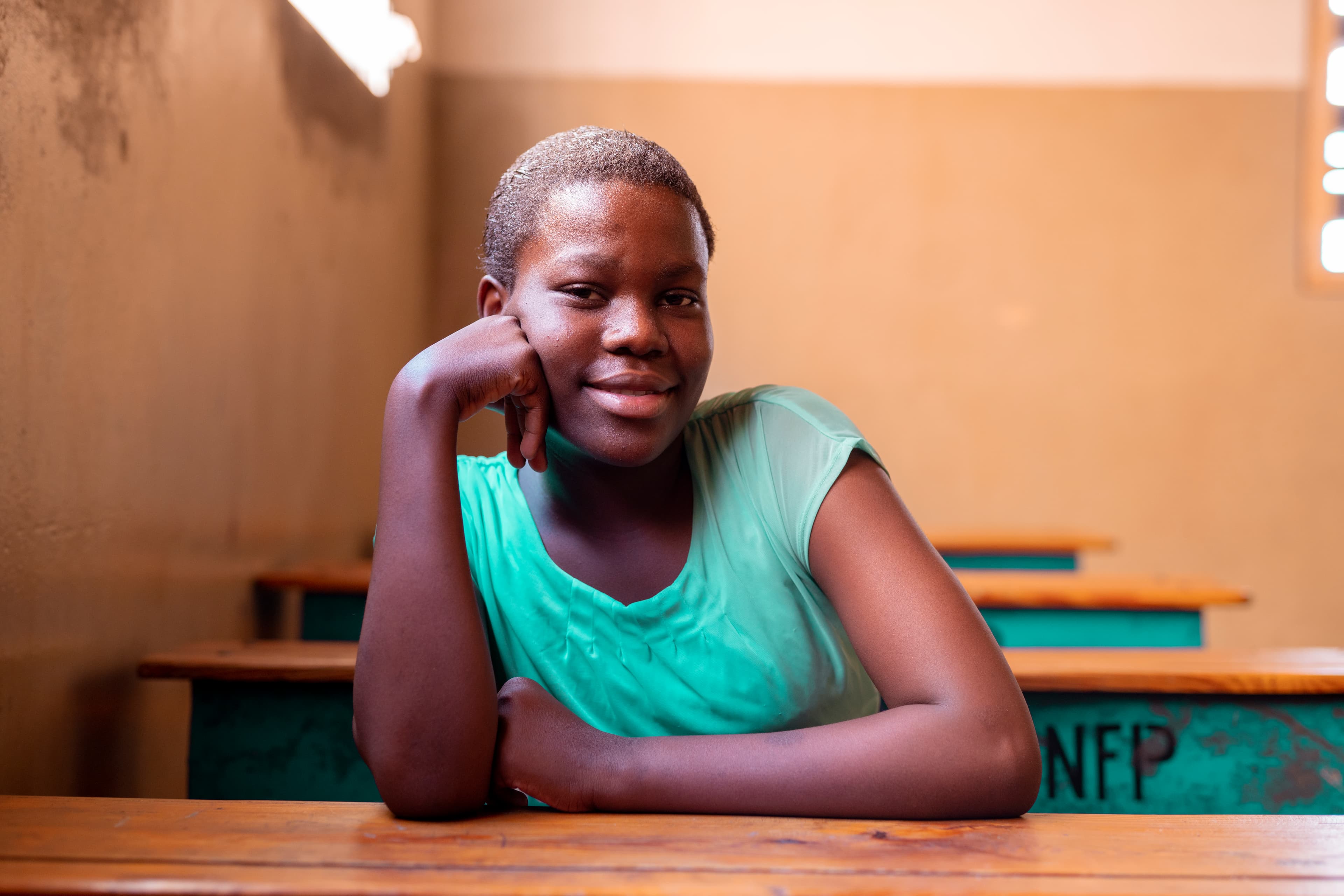 A young woman is sitting in her project classroom smiling at the camera.