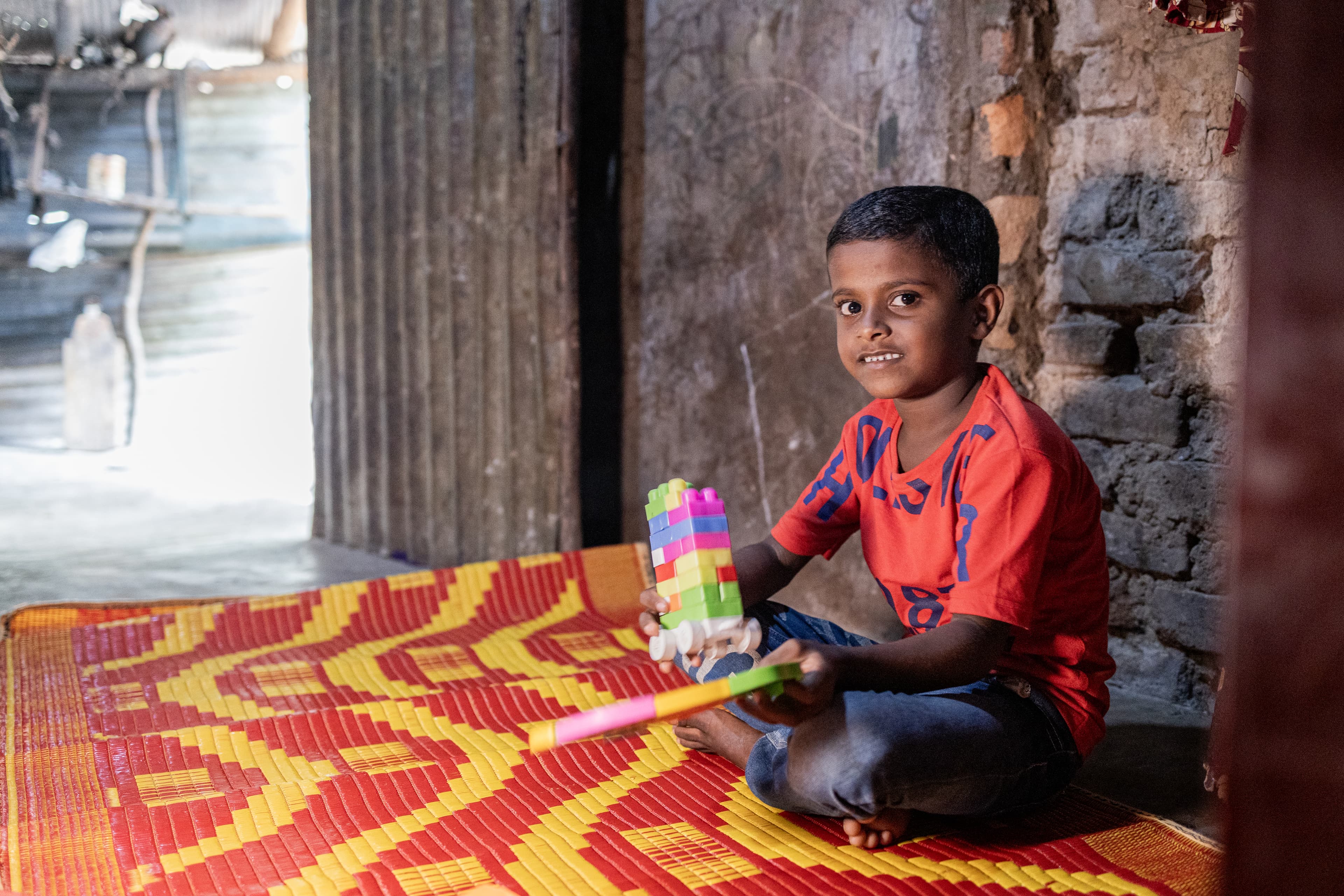 Young boy is sitting on a mat inside his home with some of his toys.
