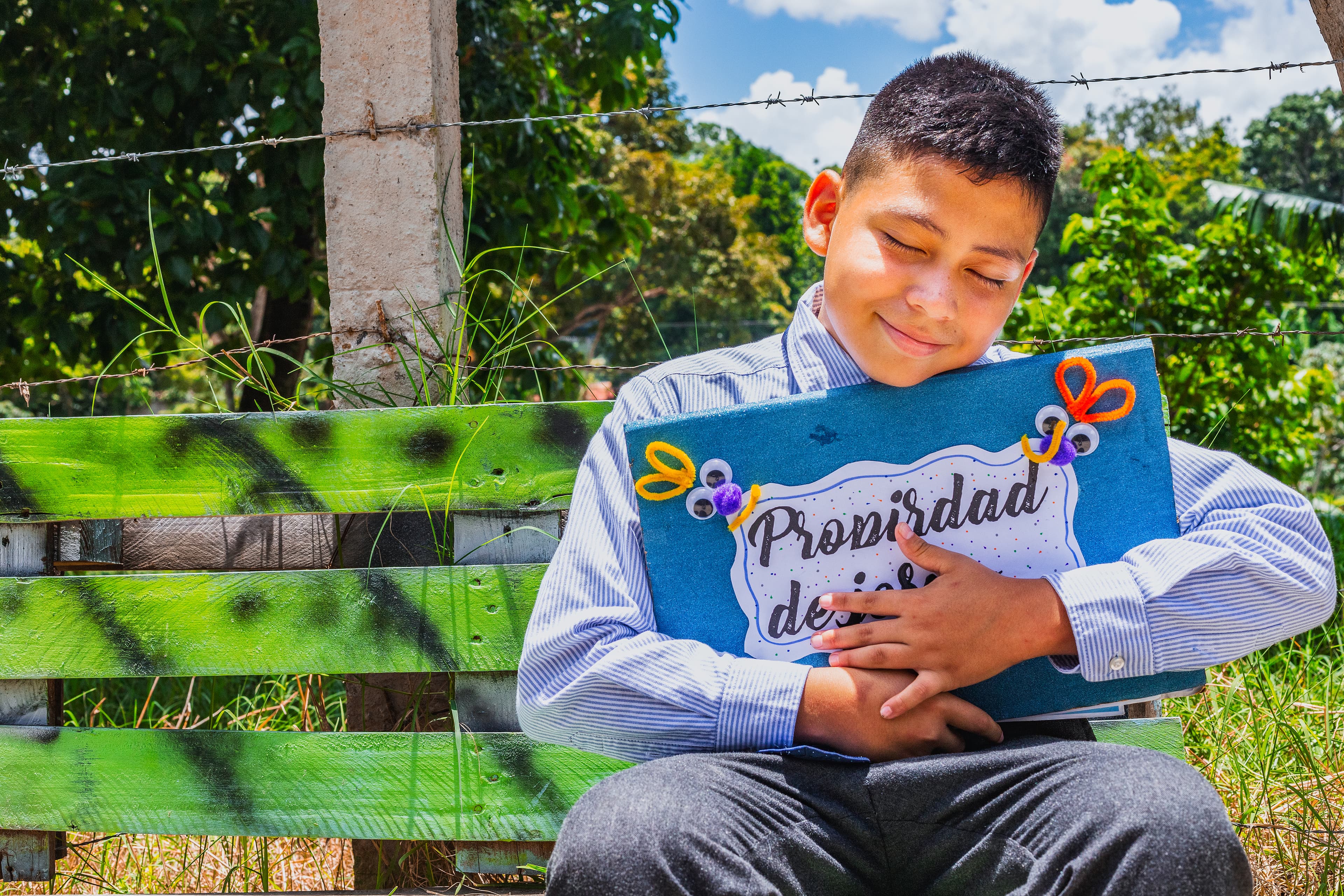 A young boy is closing his eyes and holding a blue folder he made to hold his sponsor's letters.