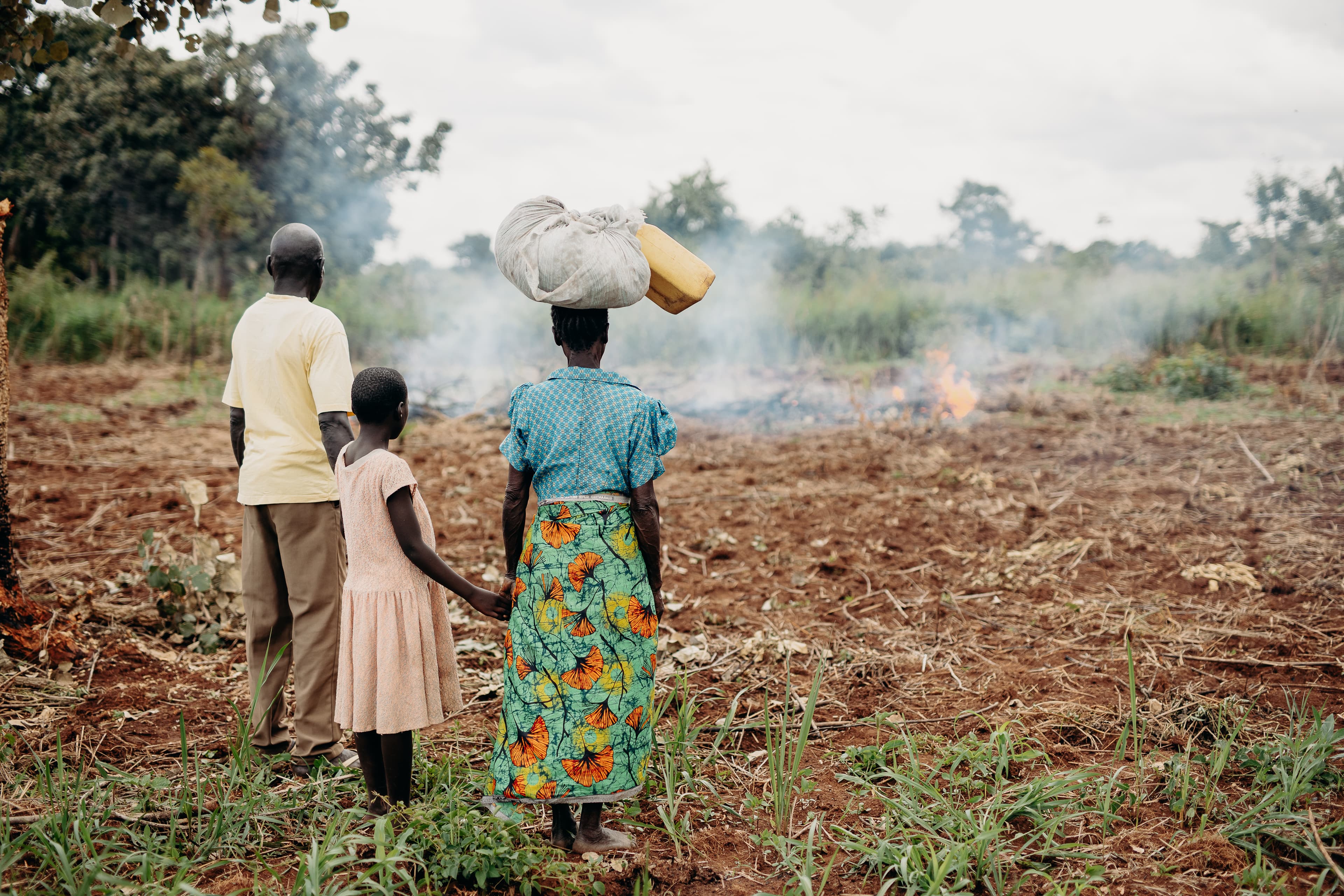 A family stands watching crops burning in the distance.