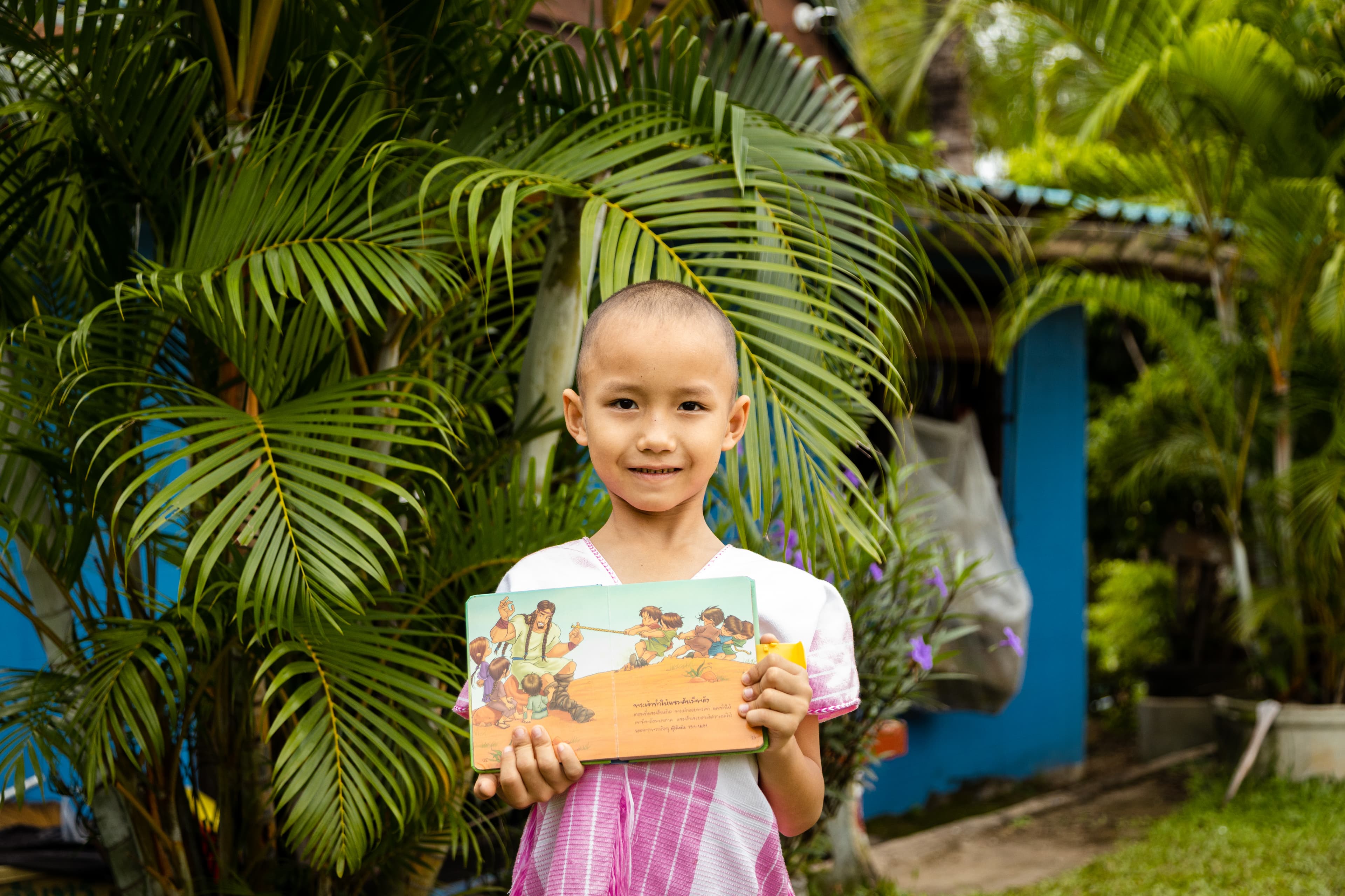 Girl stands in front of tropical trees holding a children's Bible open.