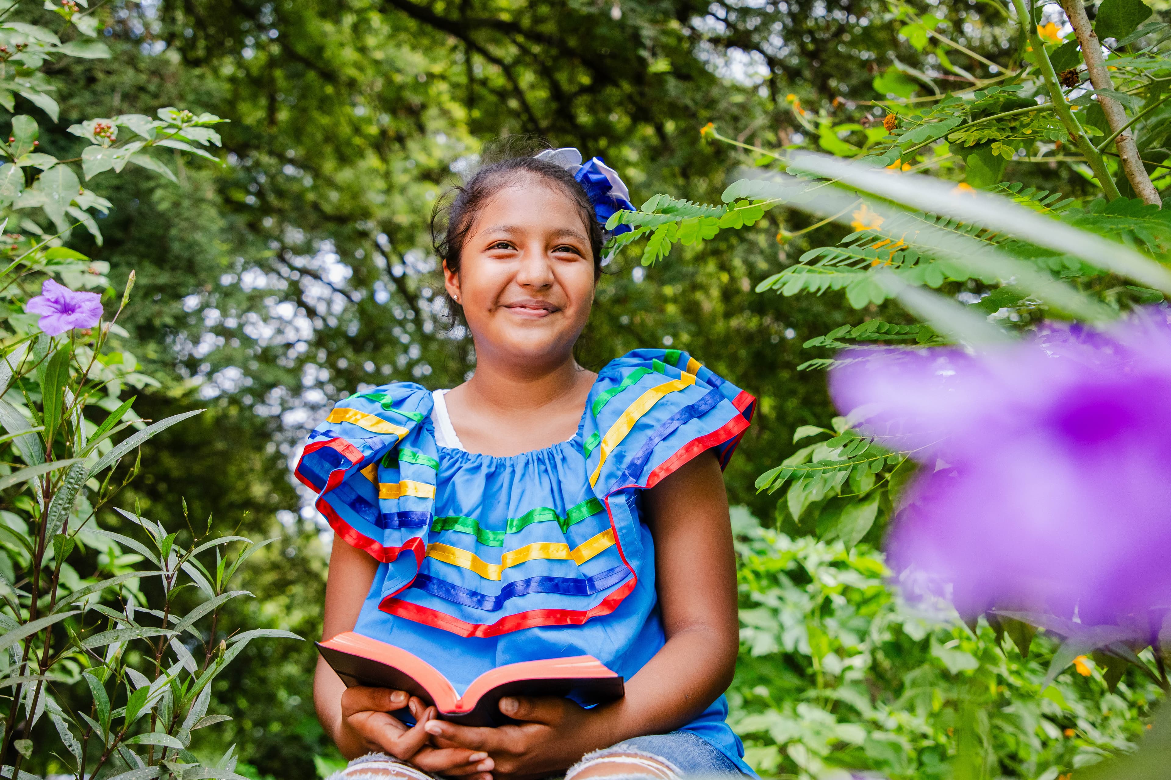 A young woman is sitting with a bible open in her lap as she smiles at the camera.