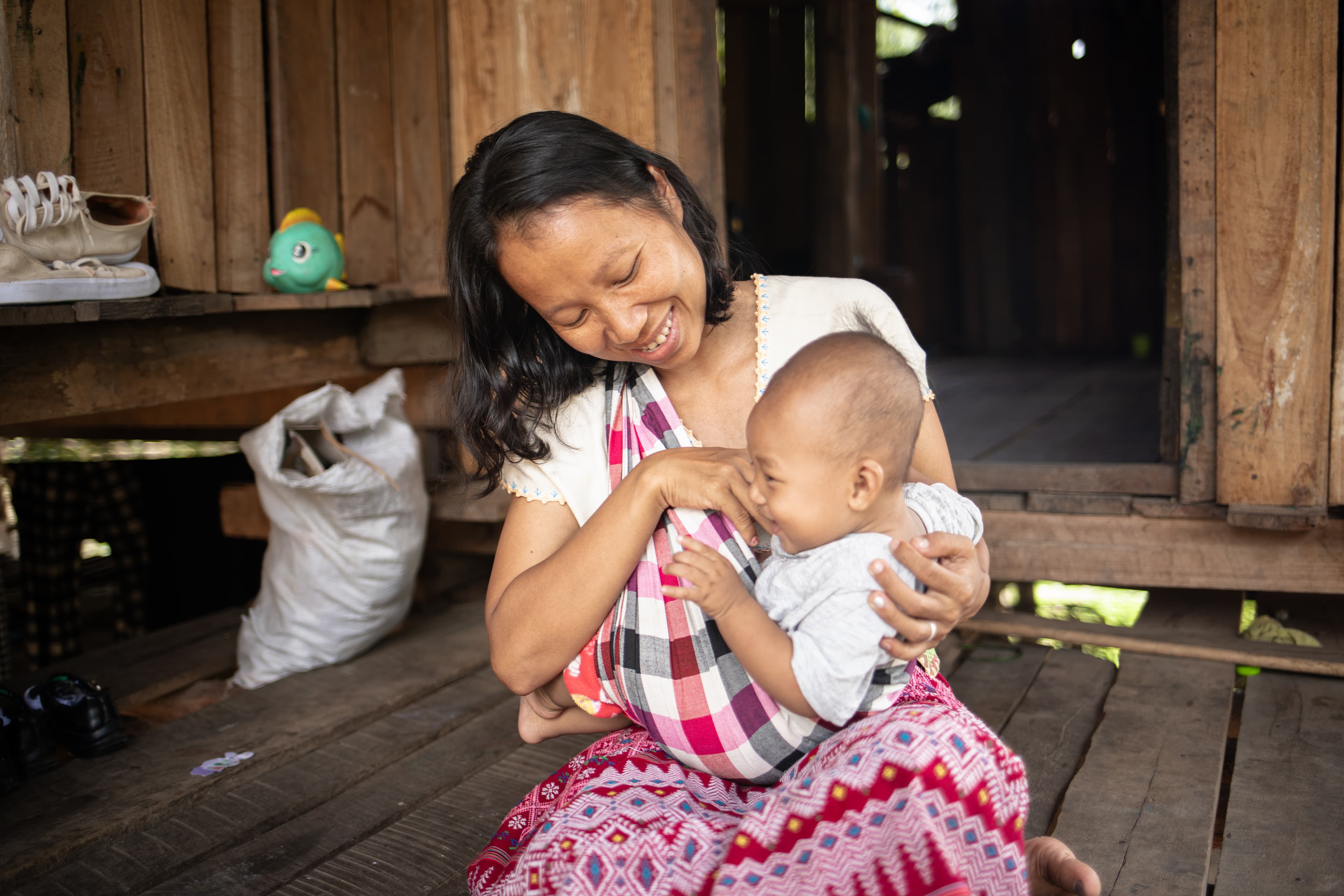 A mother is sitting and holding her child in her arms smiling.