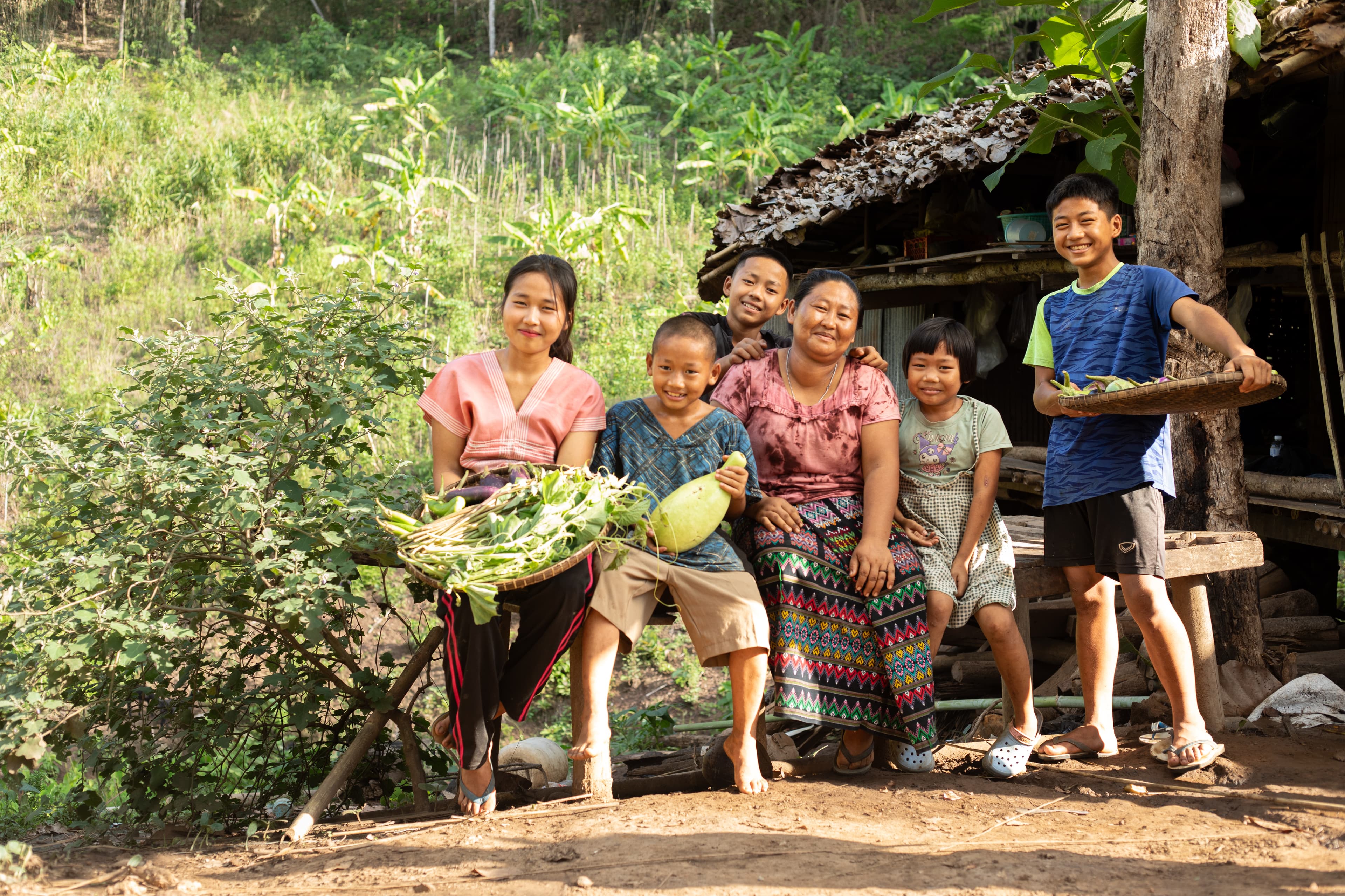 A family of six is sitting in front of their home.
