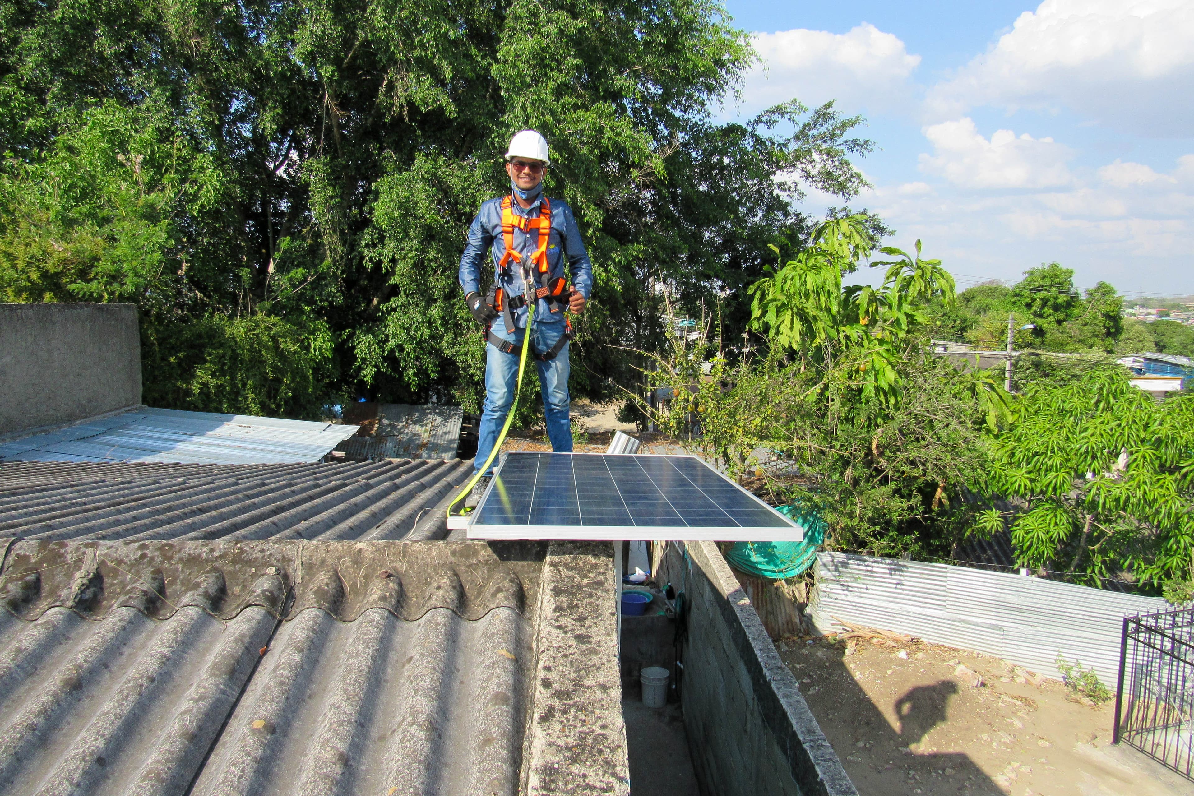 Male construction worker stands on a roof while installing solar panels.