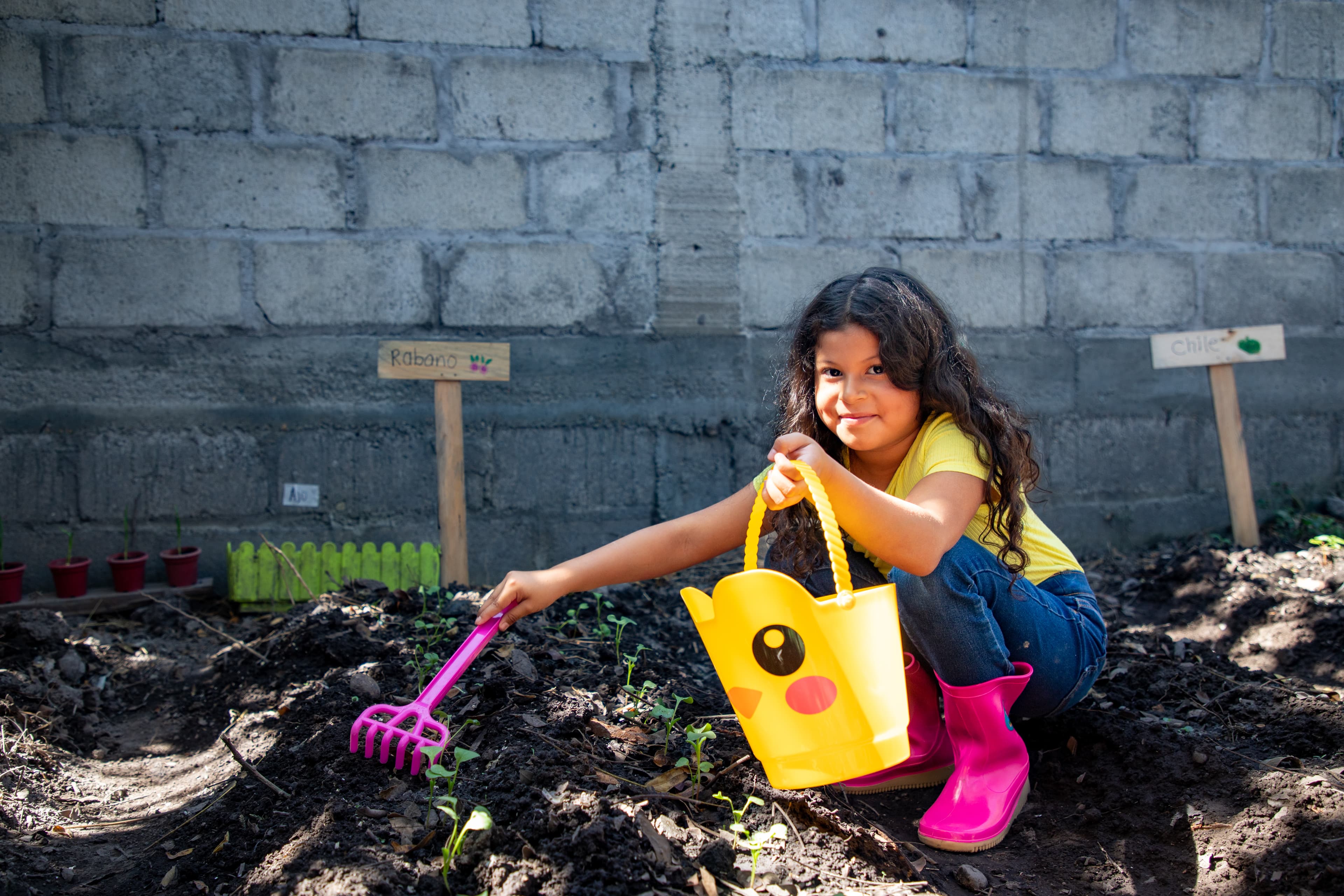 A young girl is holding a bucket as she cleans up and removes dry leaves from her garden.