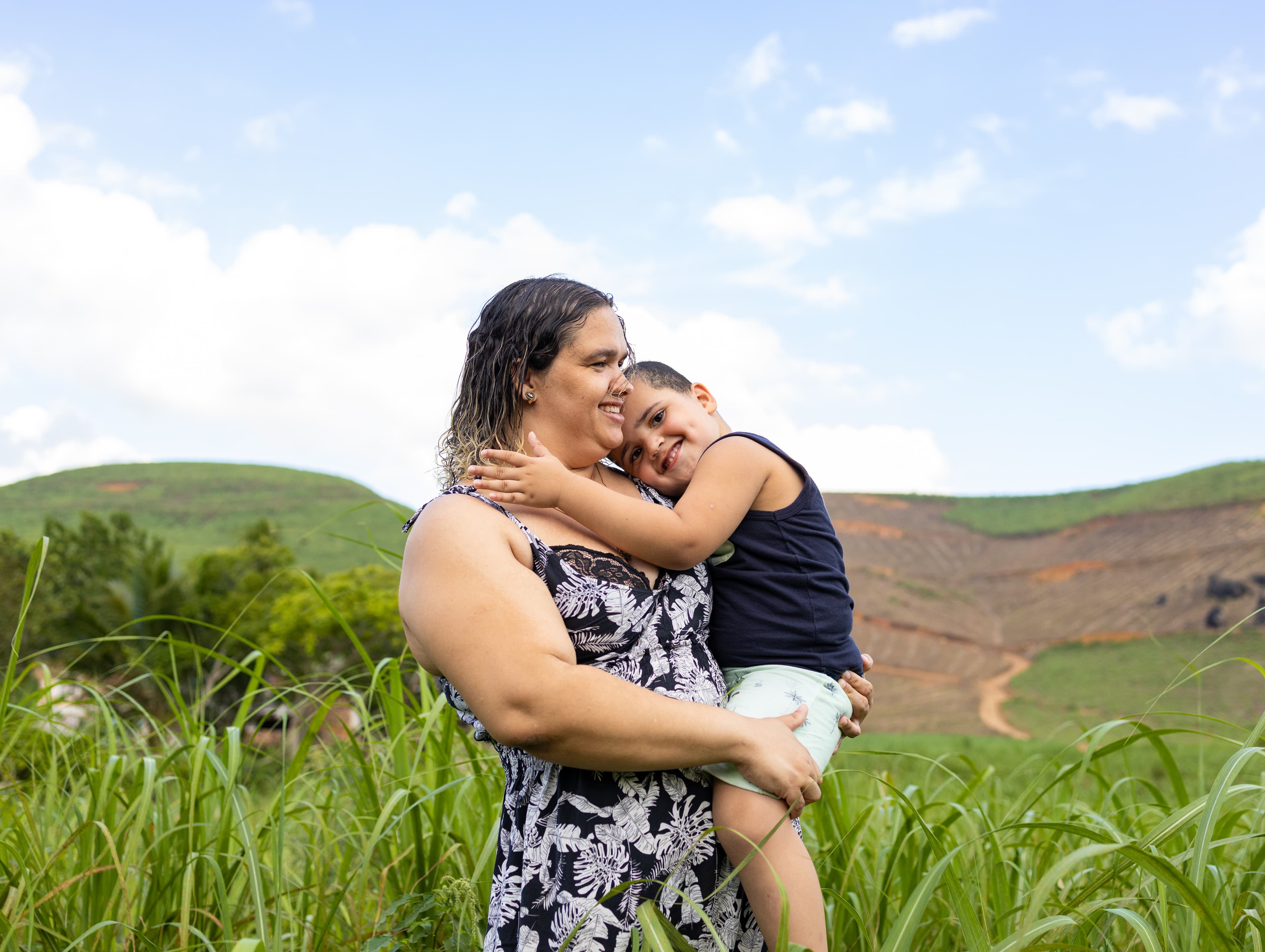 A mom holds her son in a field as they both smile.