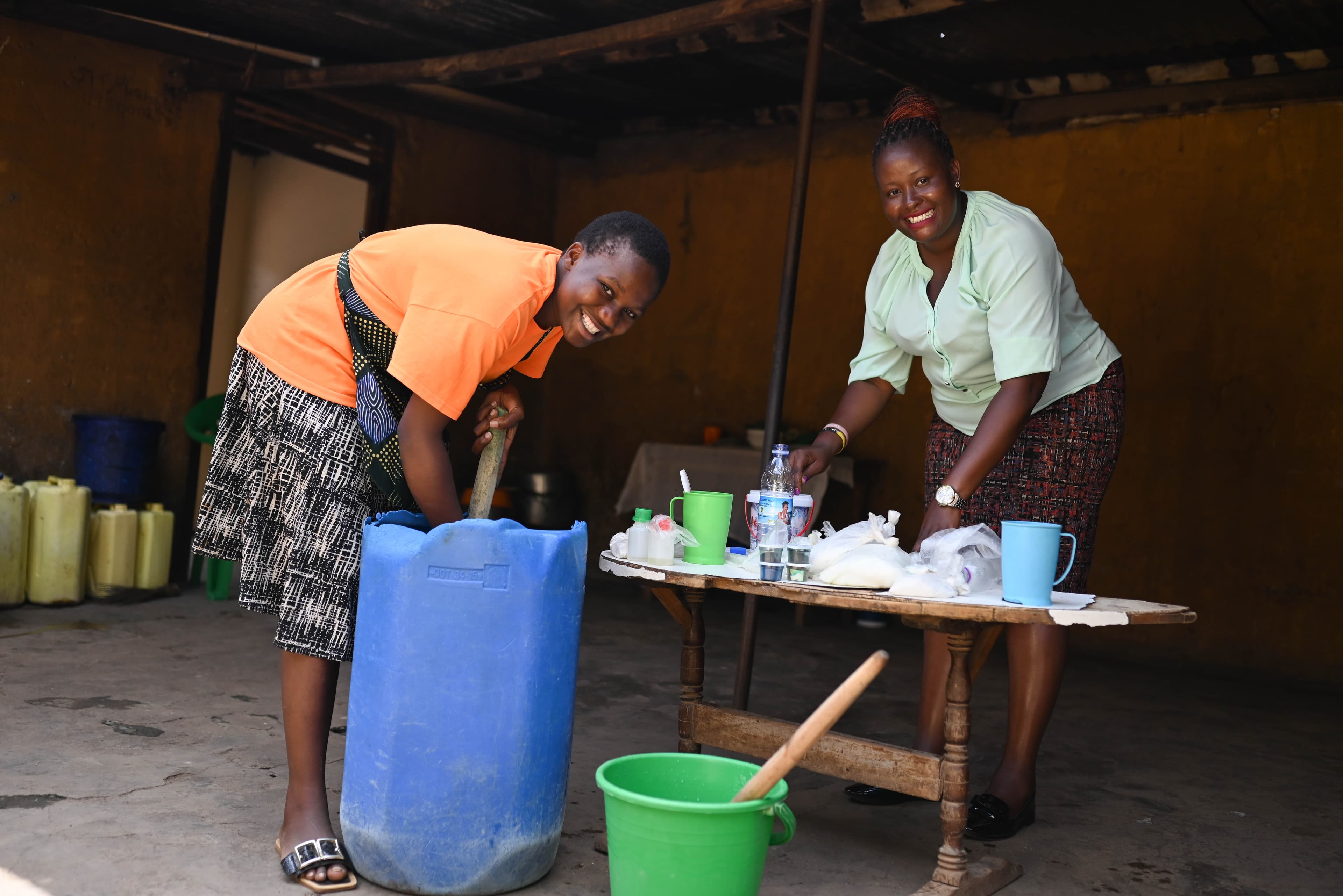 Two African woman smile for the camera while making soap.
