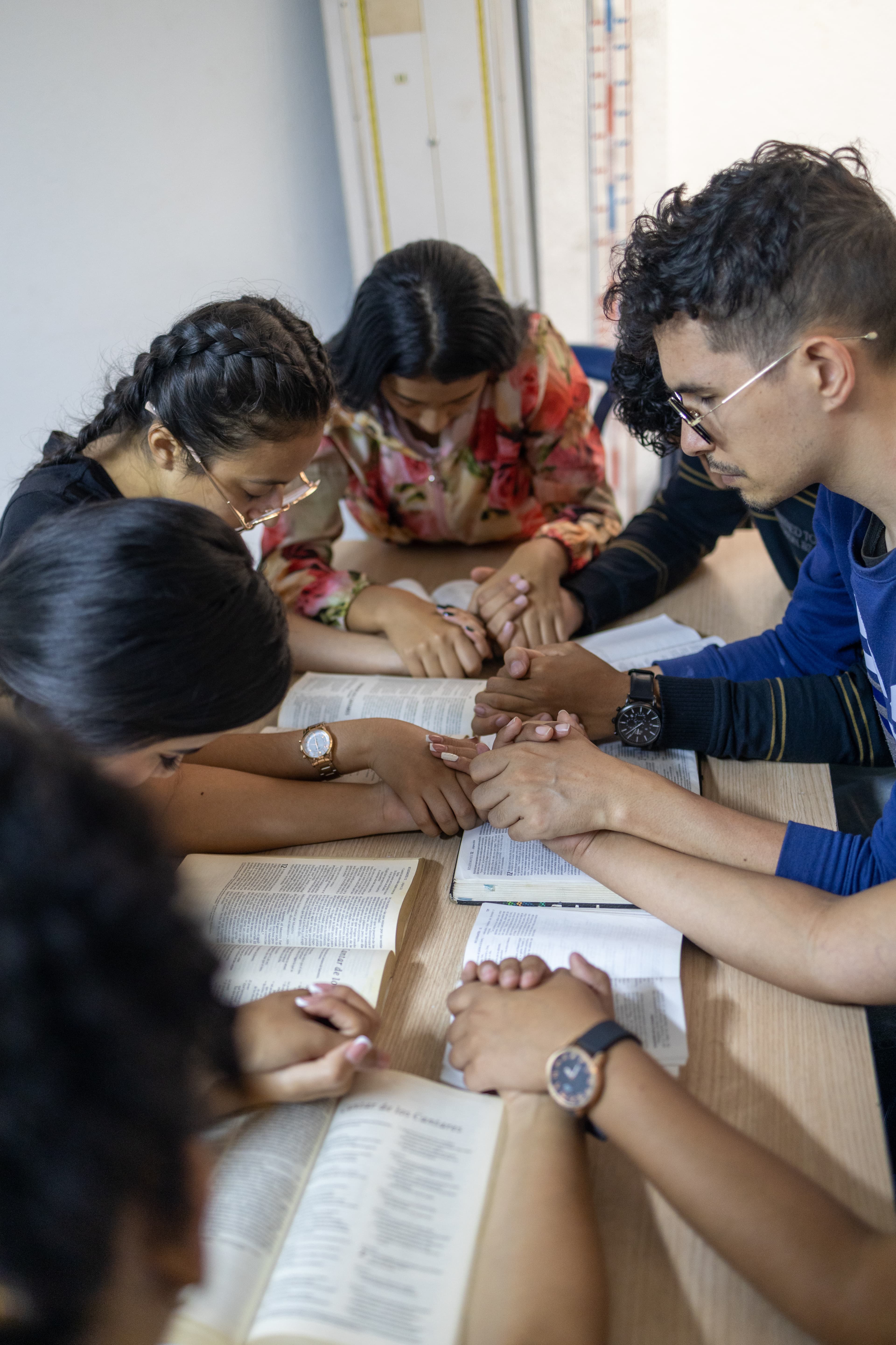 A group of young adults hold hands as they pray and study the Bible together at a Compassion Center.