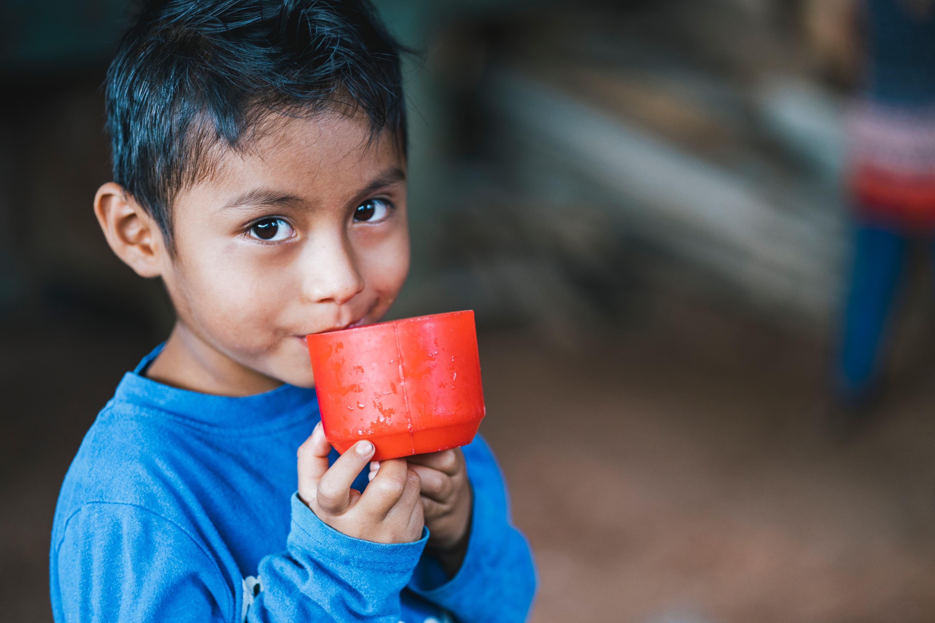 A little boy is holding a cup in his hands with a curious smile on his face.