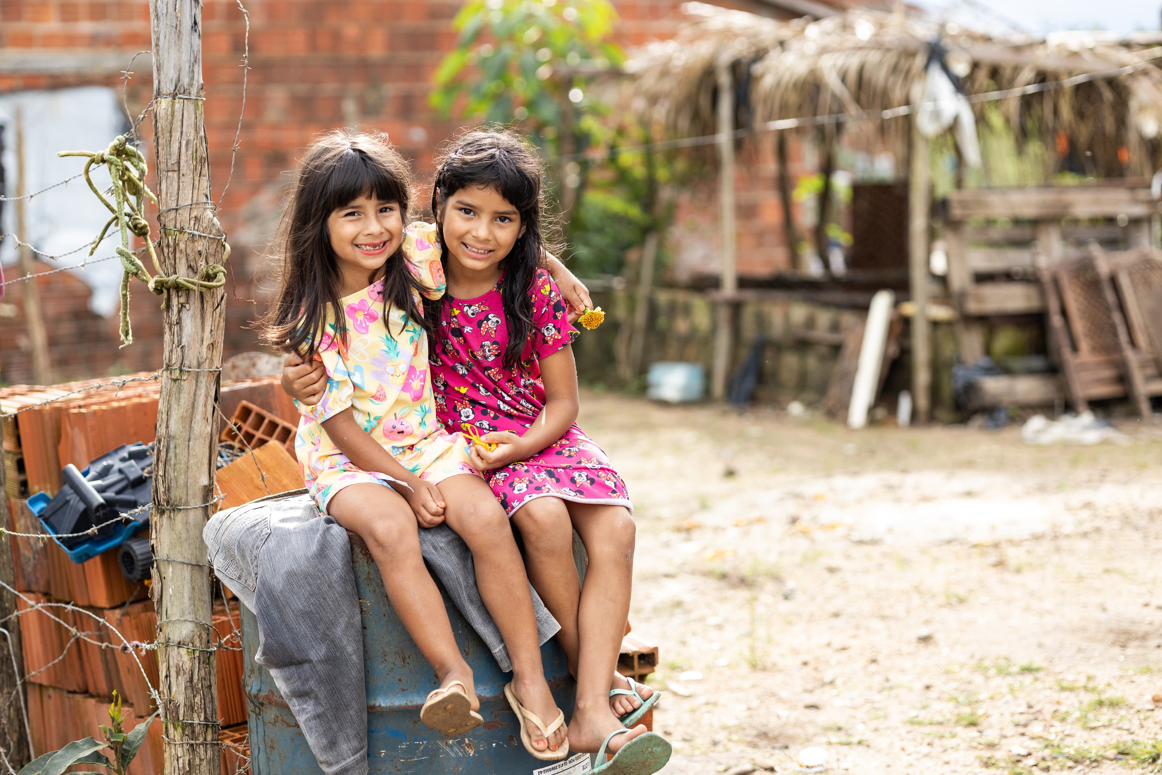 Two Brazilian girls sit with their arms wrapped around each other as they smile.