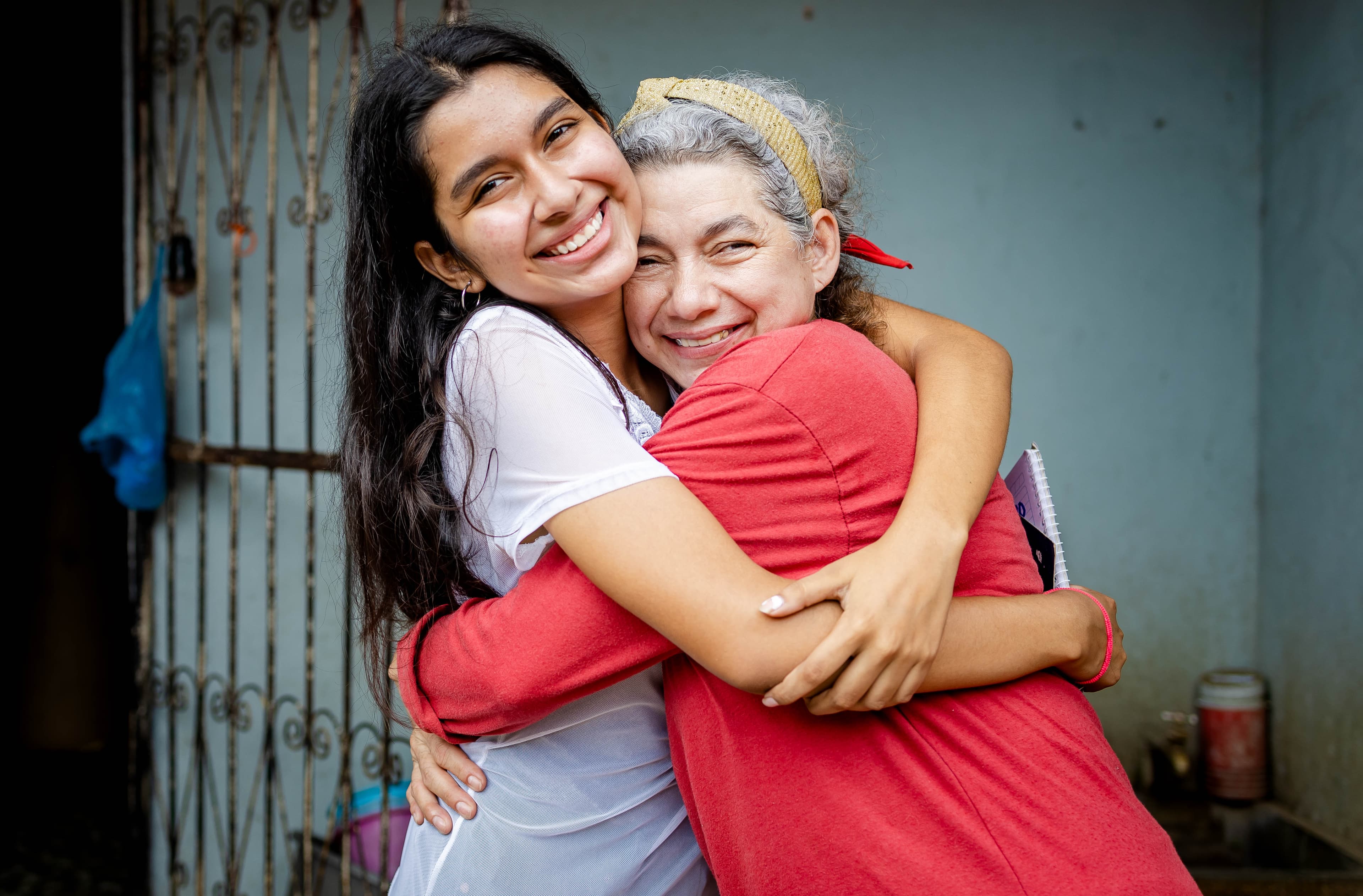 A young girl is standing outside her house, hugging her mother.