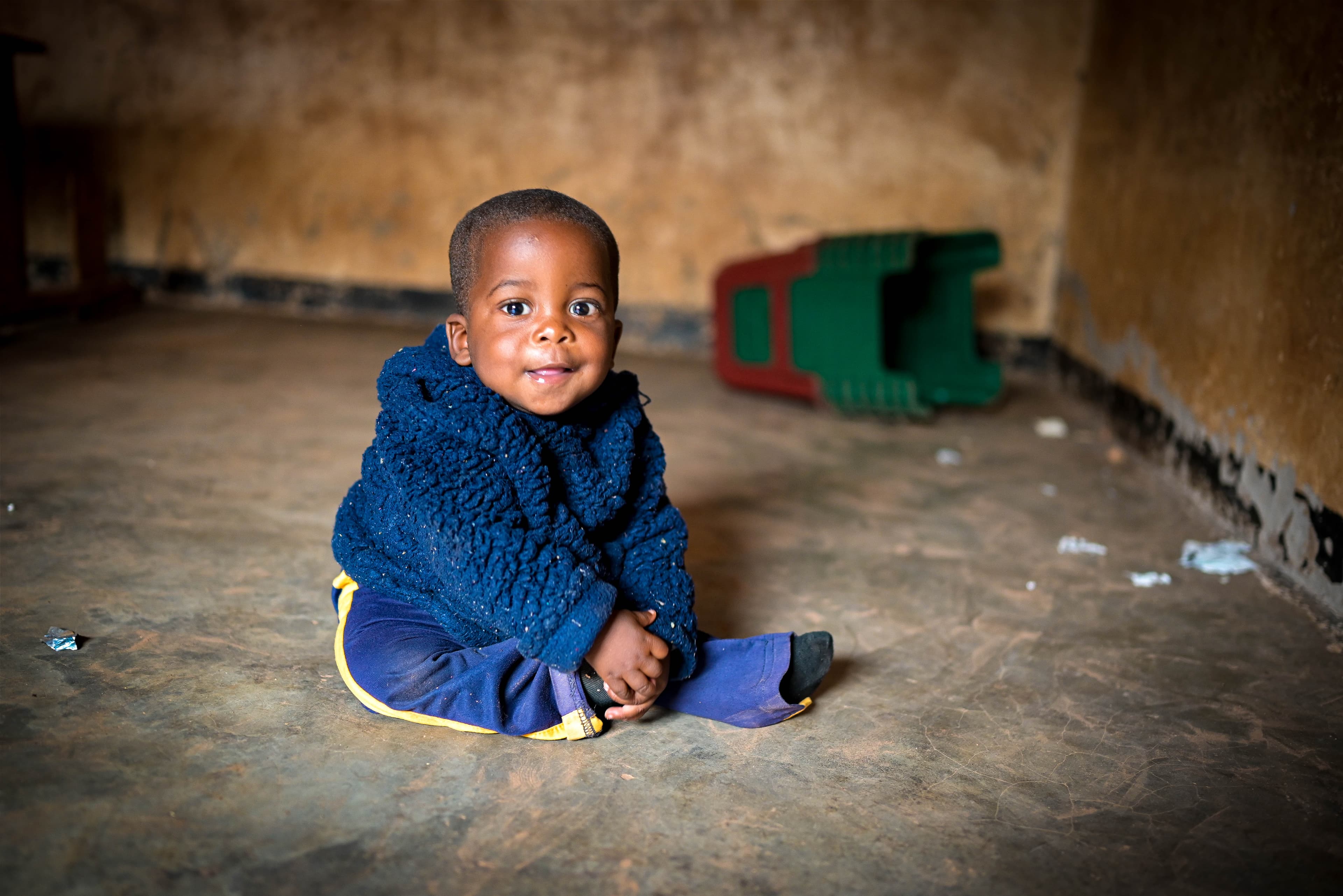 A baby boy is sitting on the ground holding his foot.