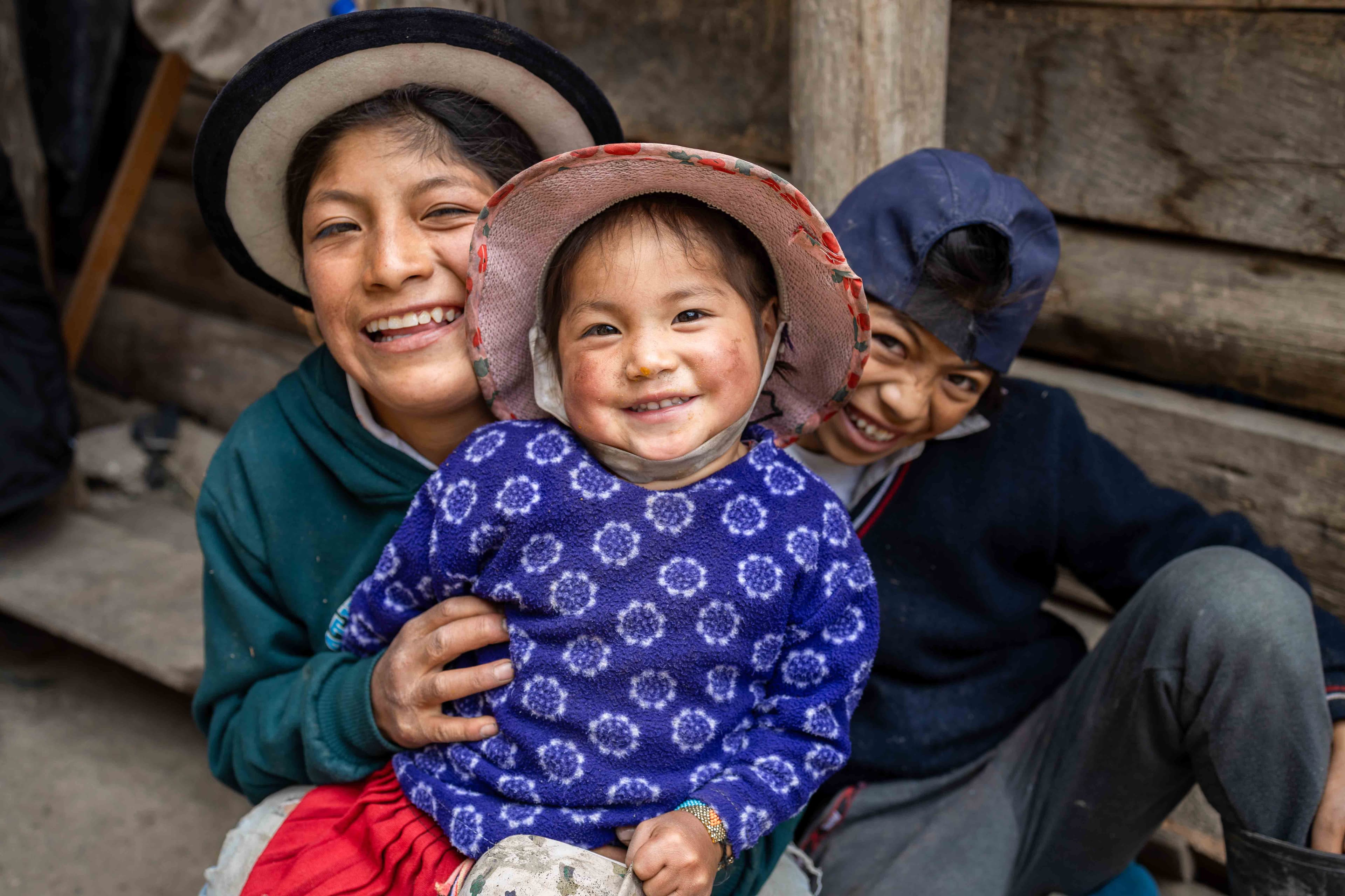 Three Ecuadorean children wearing hats smile for the camera.