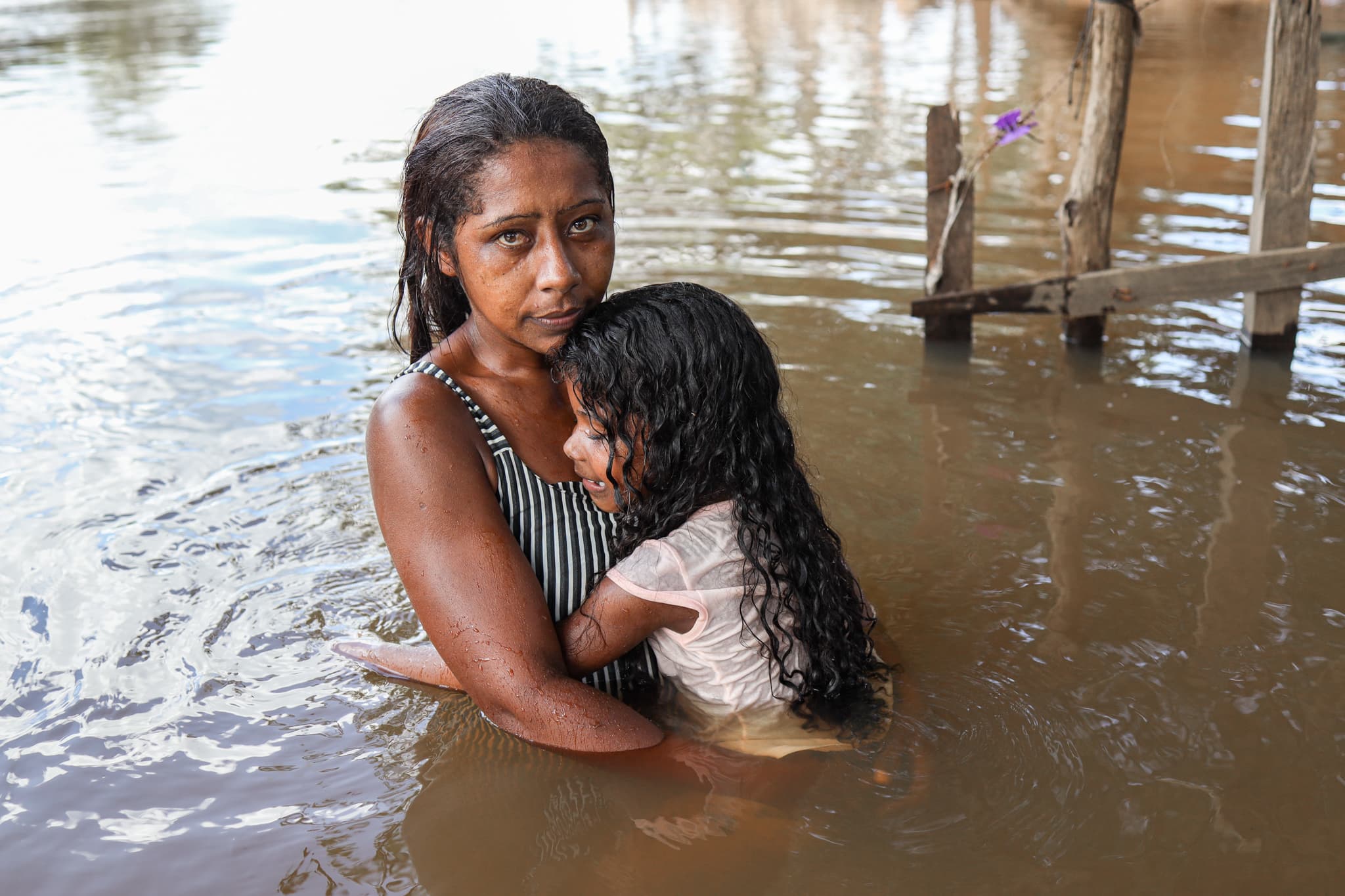 A mother standing inside a river hugging her daughter.