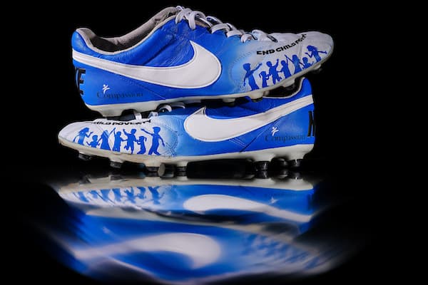 Blue and white cleats featuring "End Child Poverty" and Compassion on a black background.