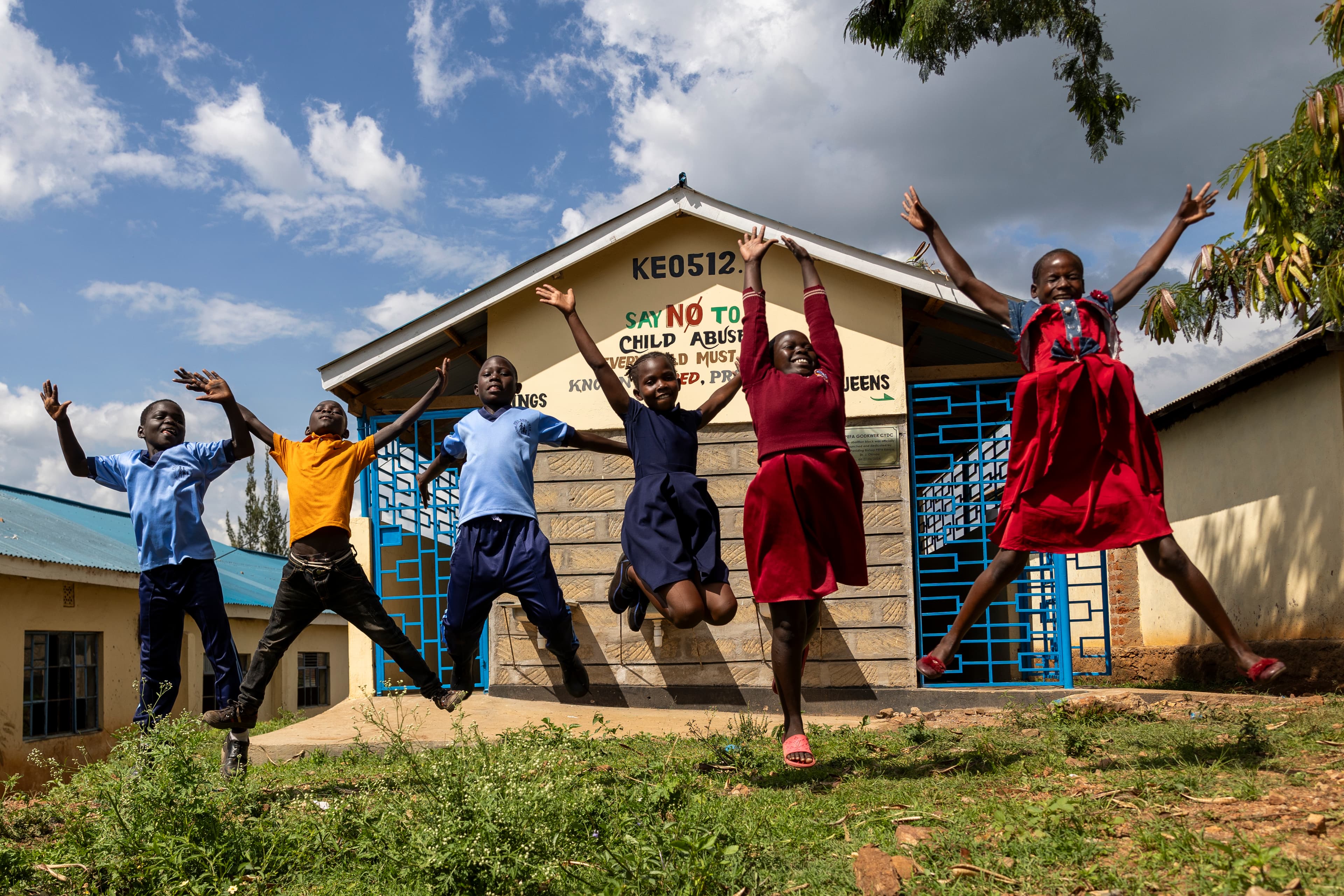 Six children are smiling and jumping in the air outside their church building.