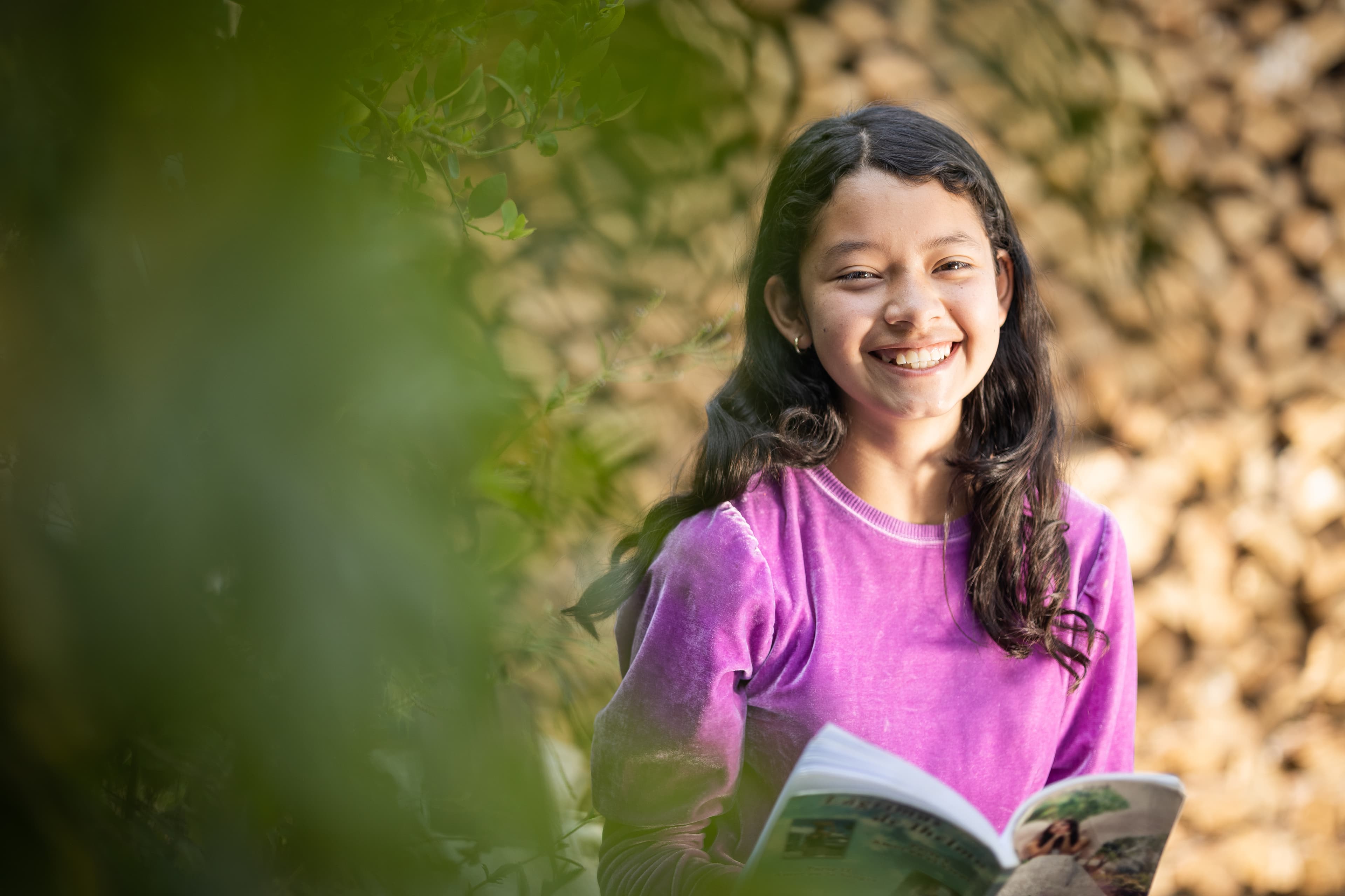 A young girl is holding a book and laughing as she smiles at the camera.