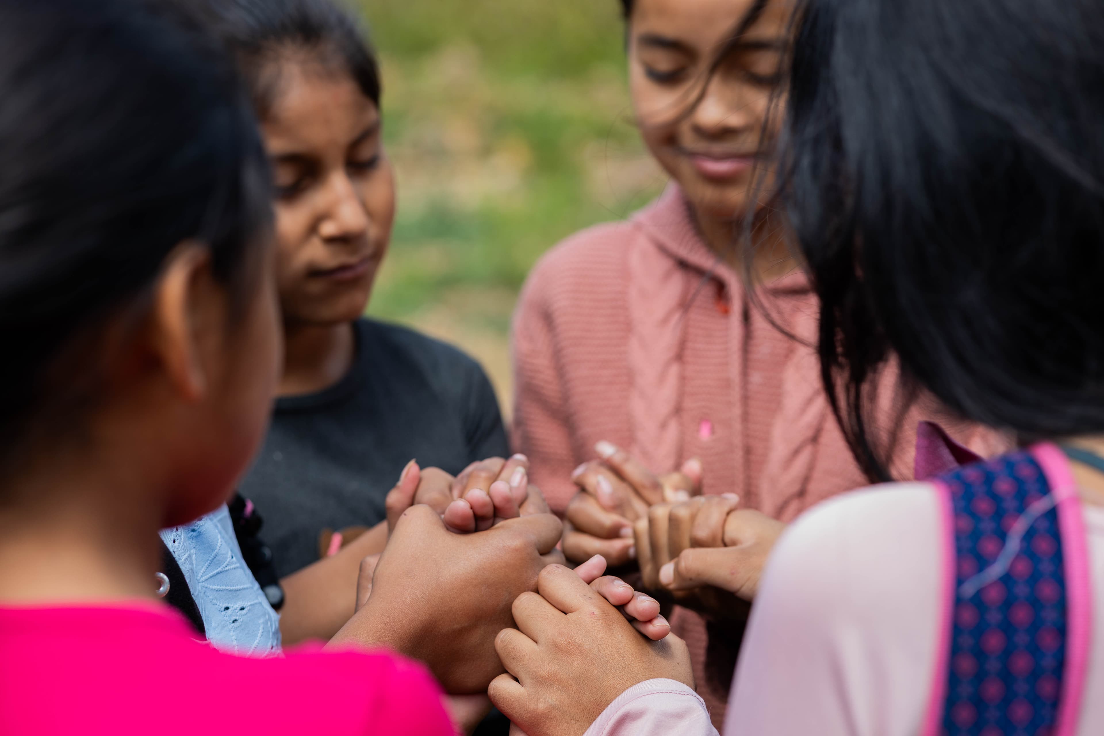 A group of girls hold hands and pray together outside.