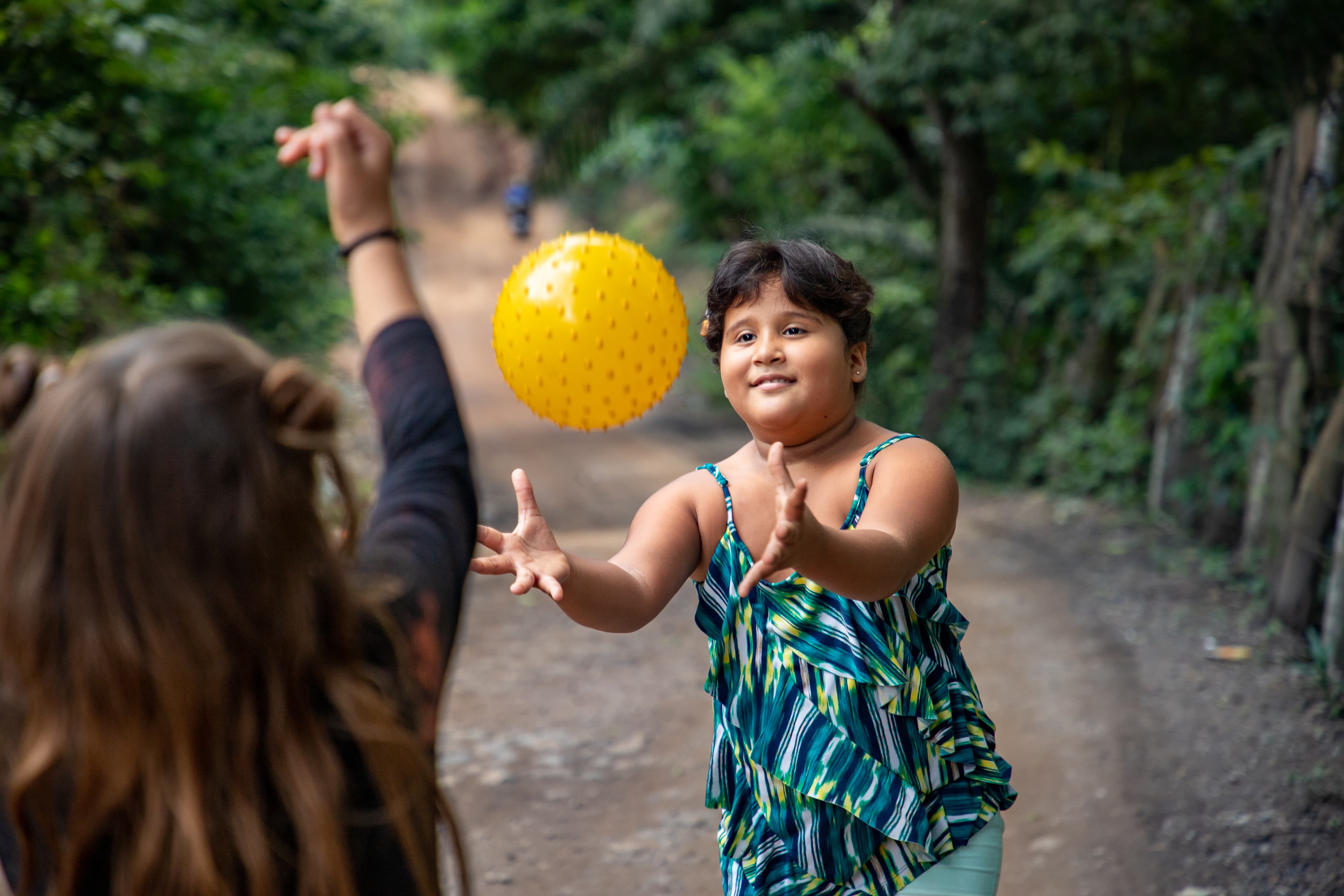 A young Honduran girl catches a yellow ball while smiling.