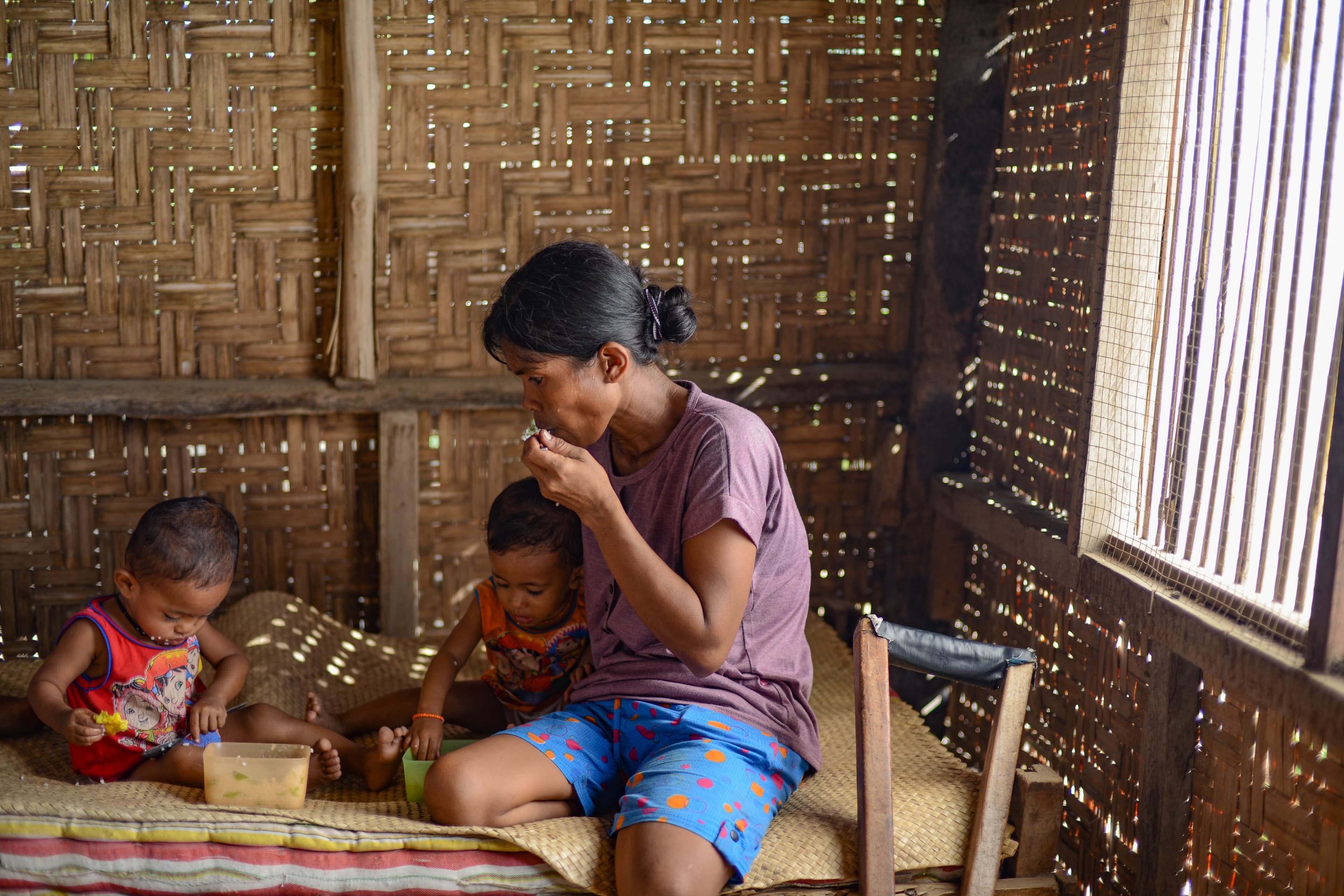 A mother is sitting with her two children on a bed inside of their home.