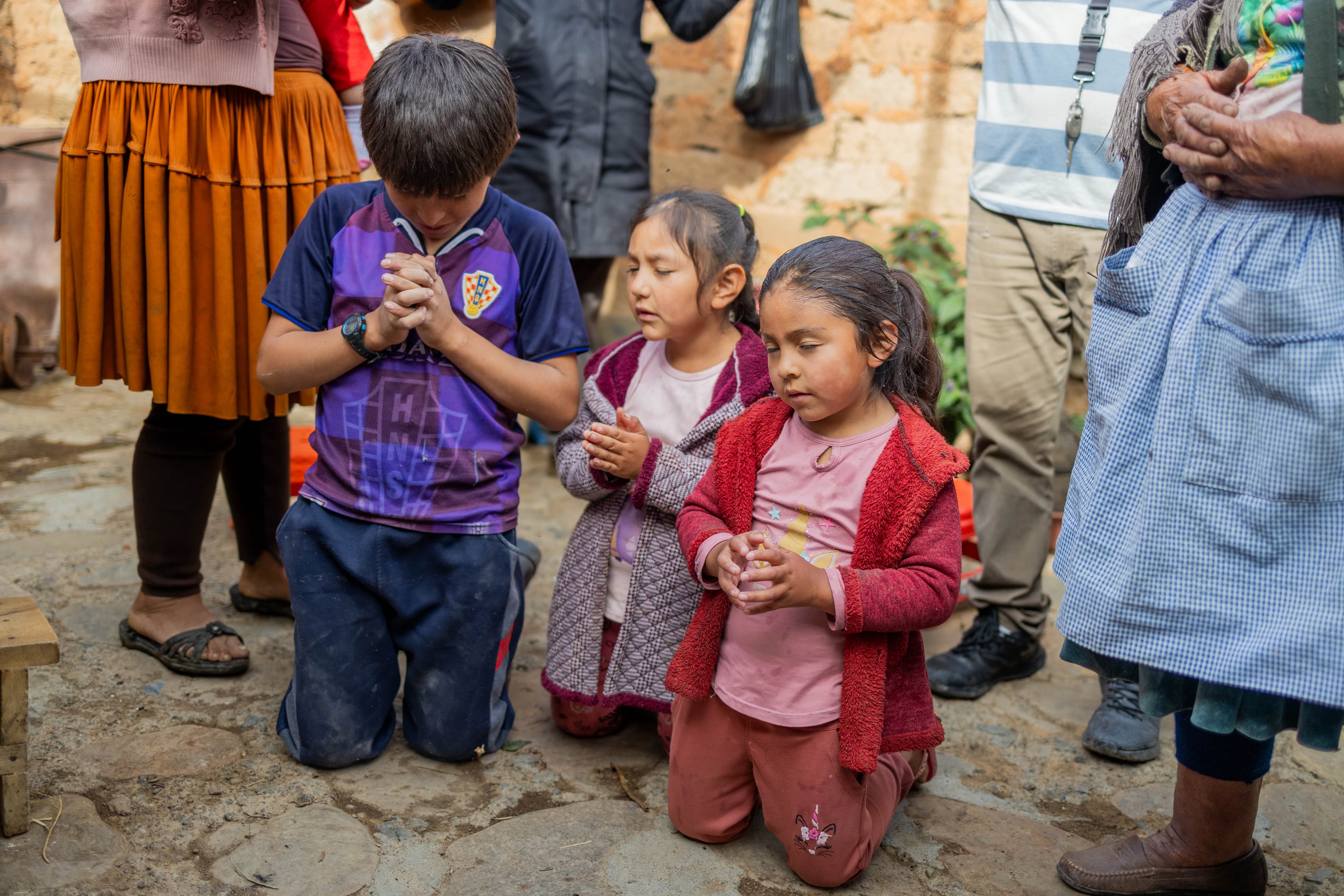 Three young children kneel on their knees and pray.