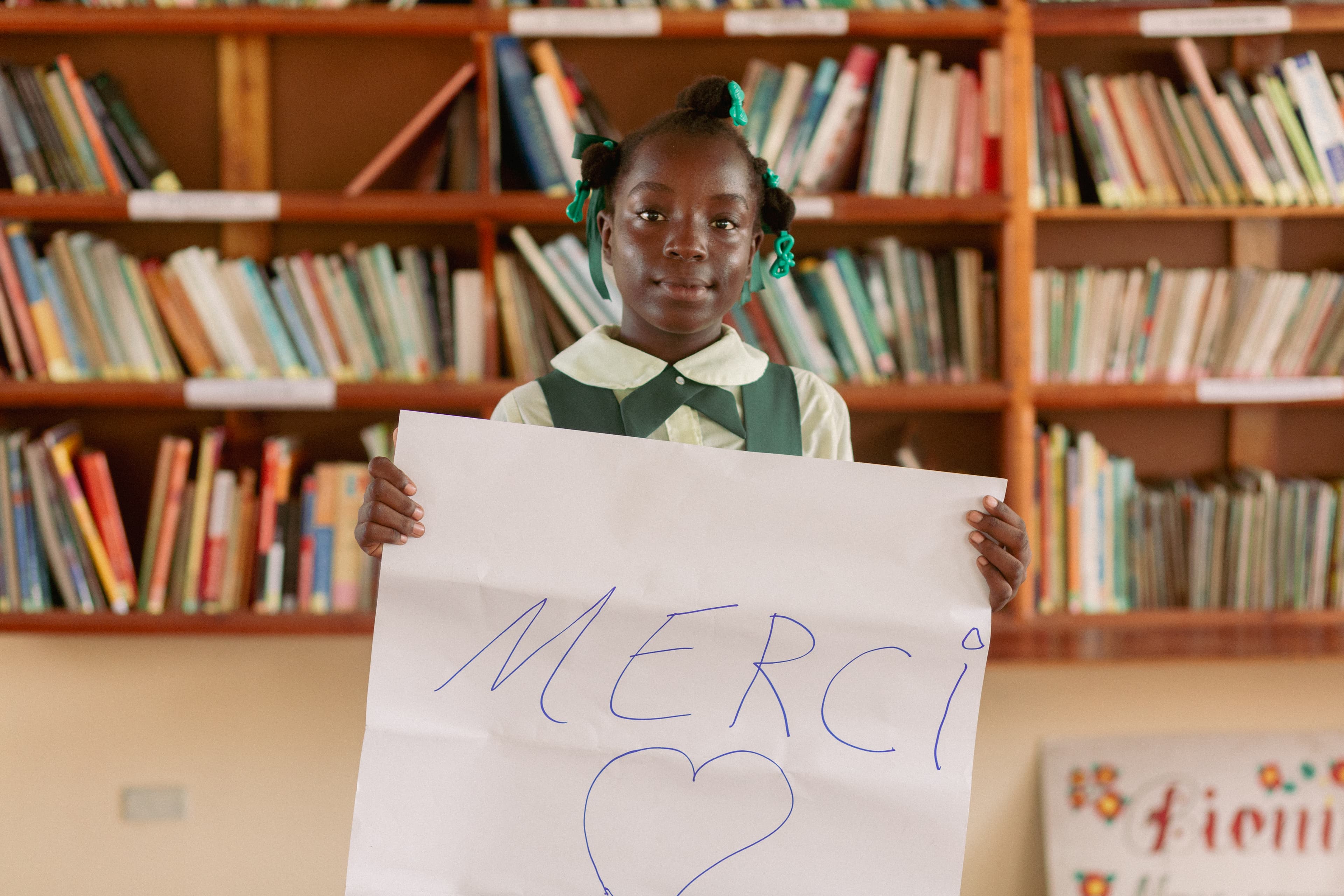 A young African girl holds up a sign that says merci