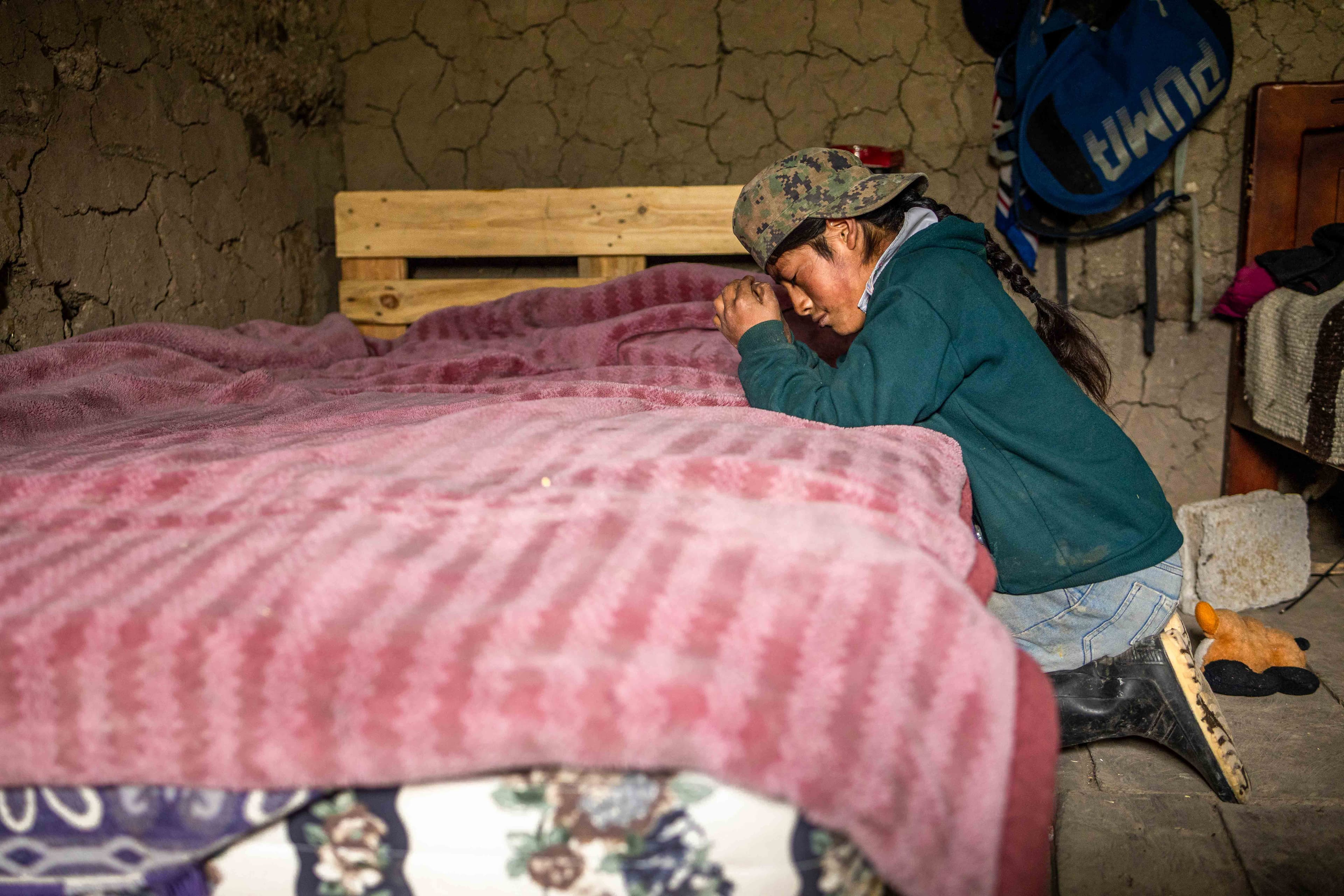A teen Ecuadorean boy kneels by his bed while praying.