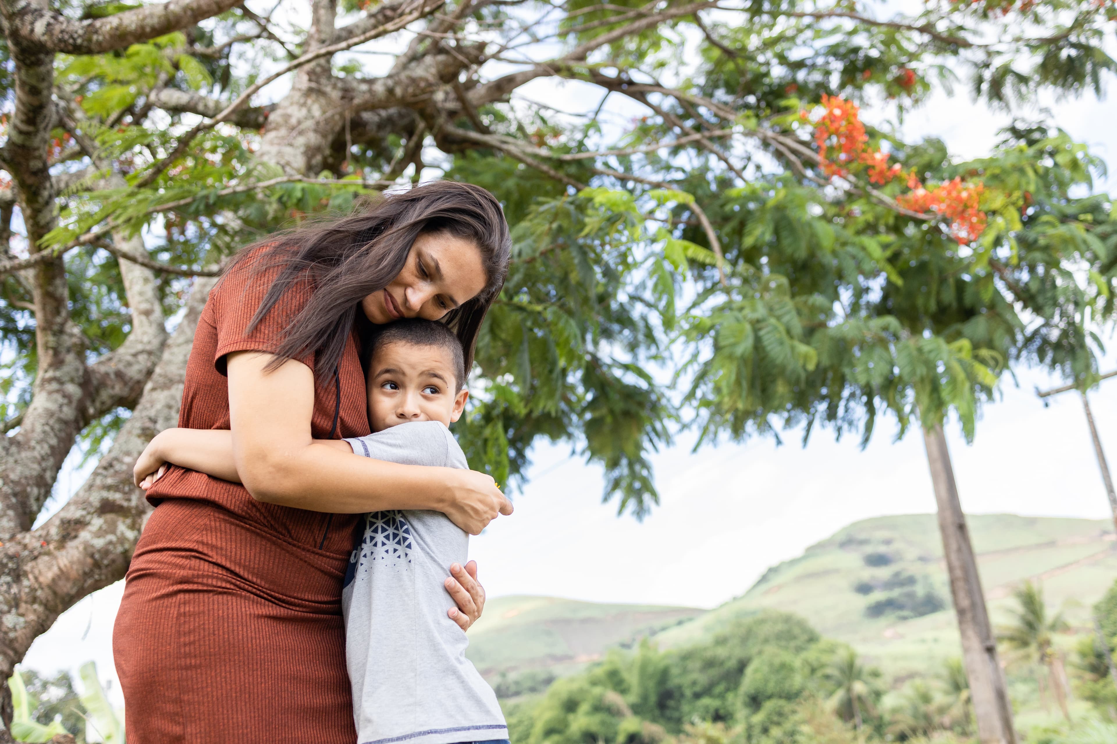 A young woman embraces a young boy as he looks off into the distance.