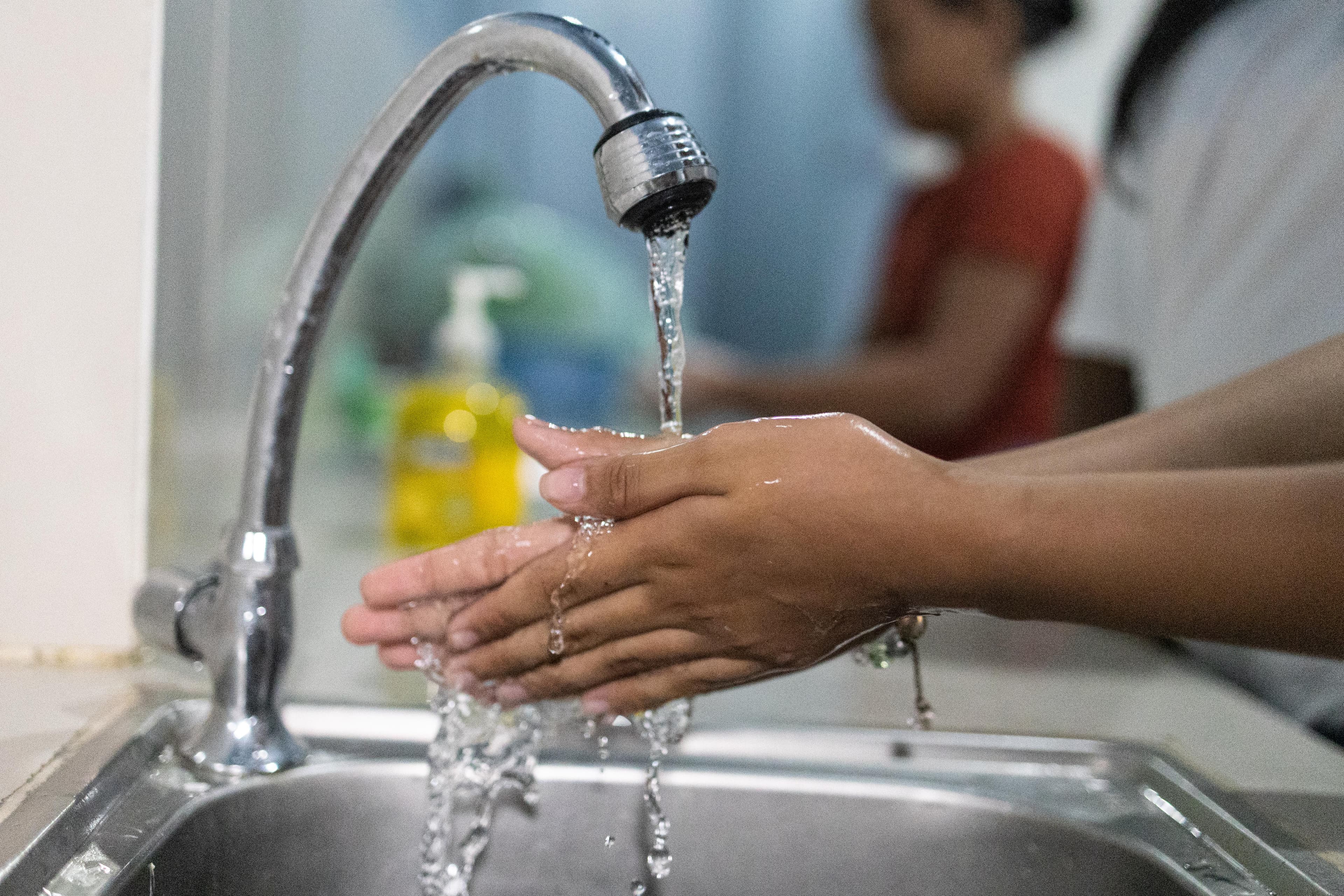 Hands being washed under a silver faucet.