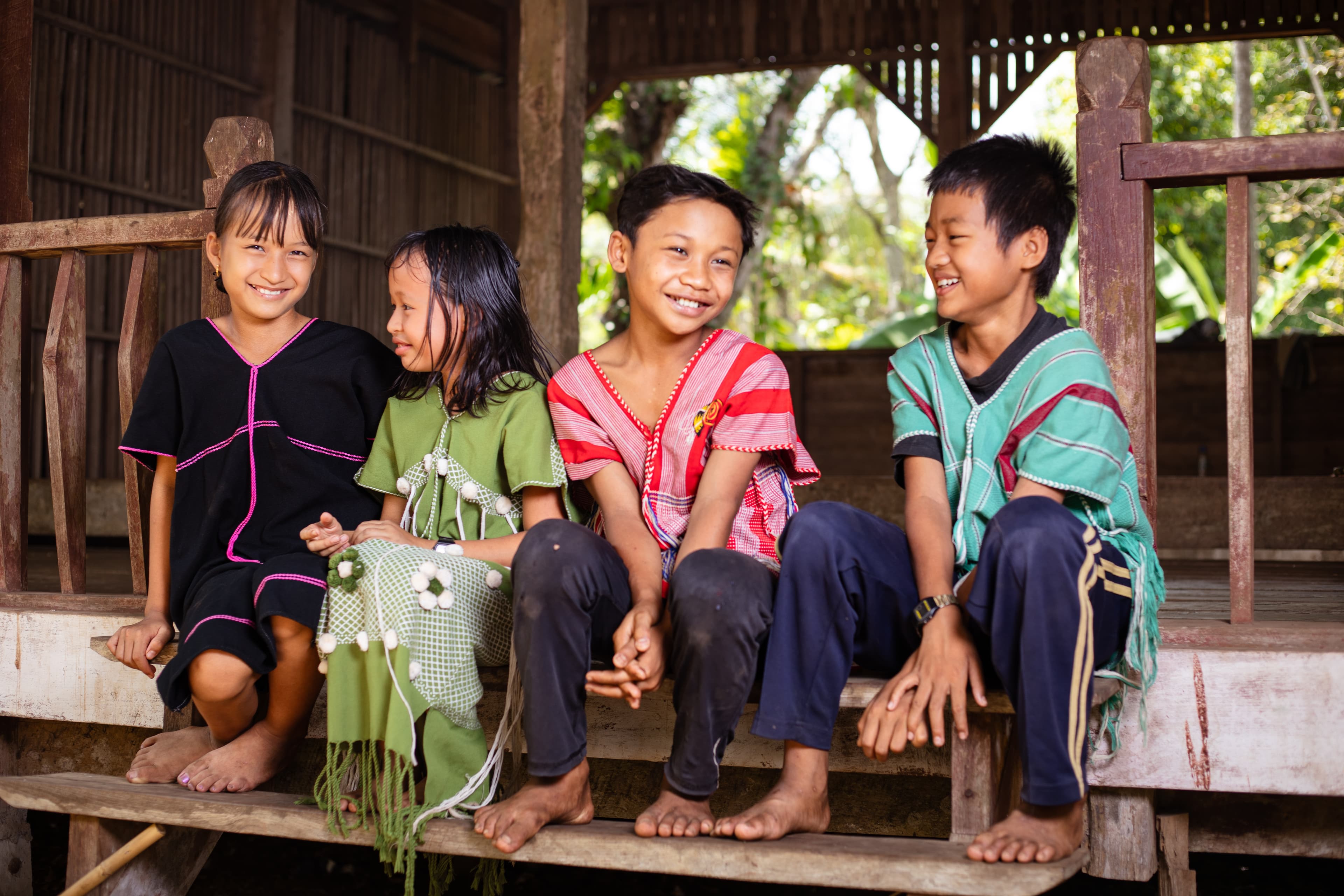 Four Thai children sit on a step and smile.