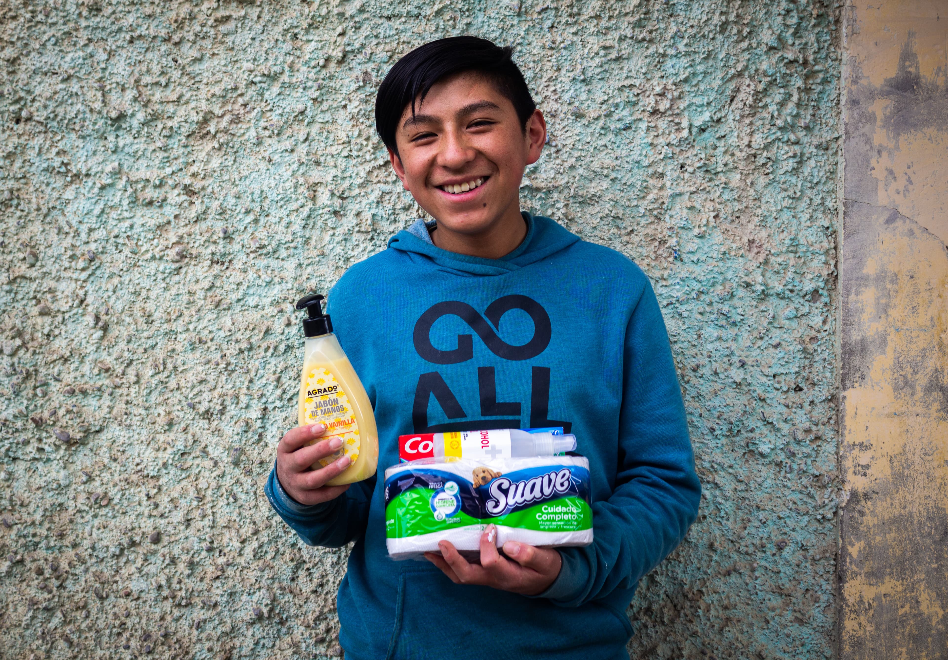 Teenaged boy in a blue sweatshirt smiles while holding soap, tissue and toothpaste.