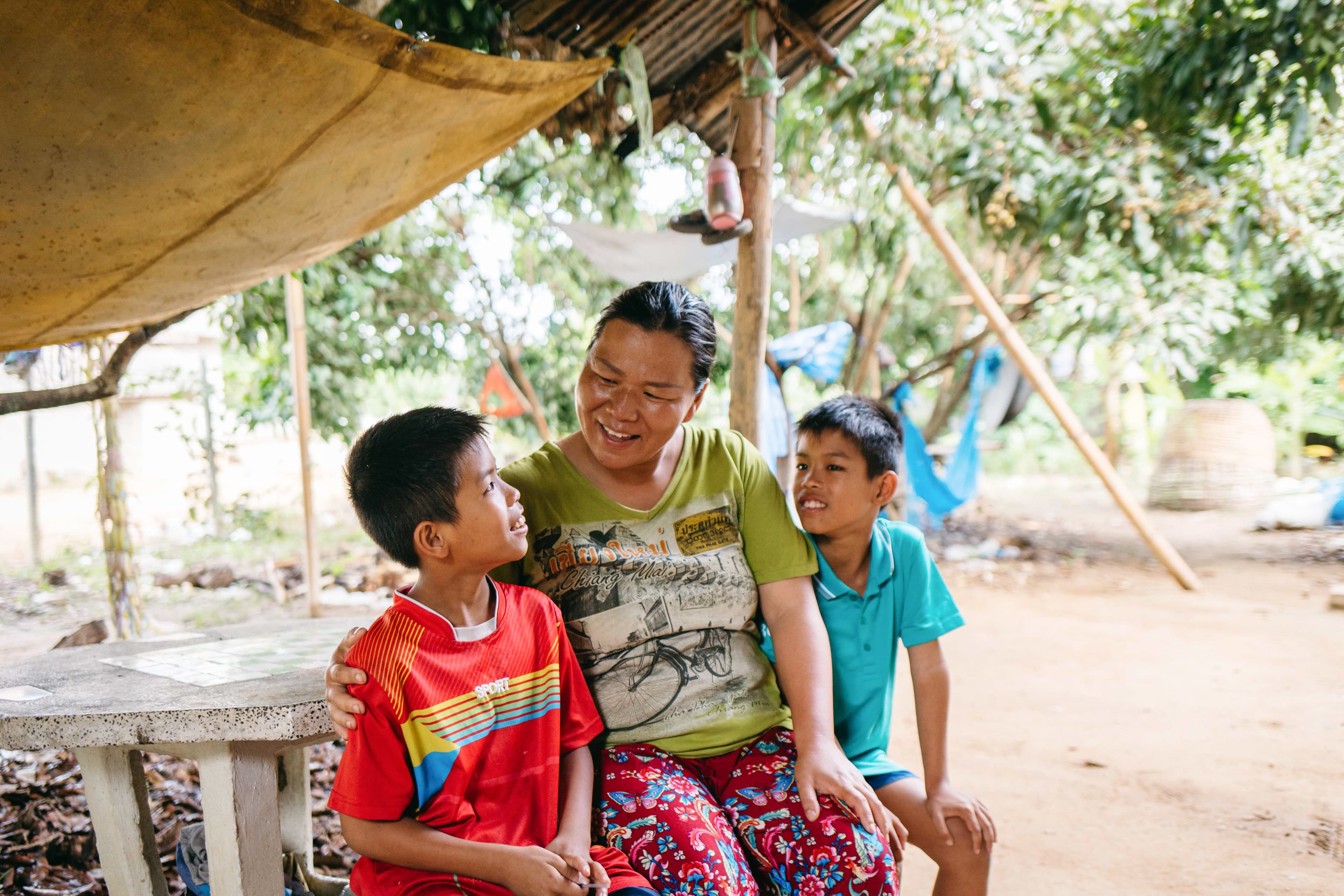 A mother is smiling as she sits with her twin boys, one on each side of her.
