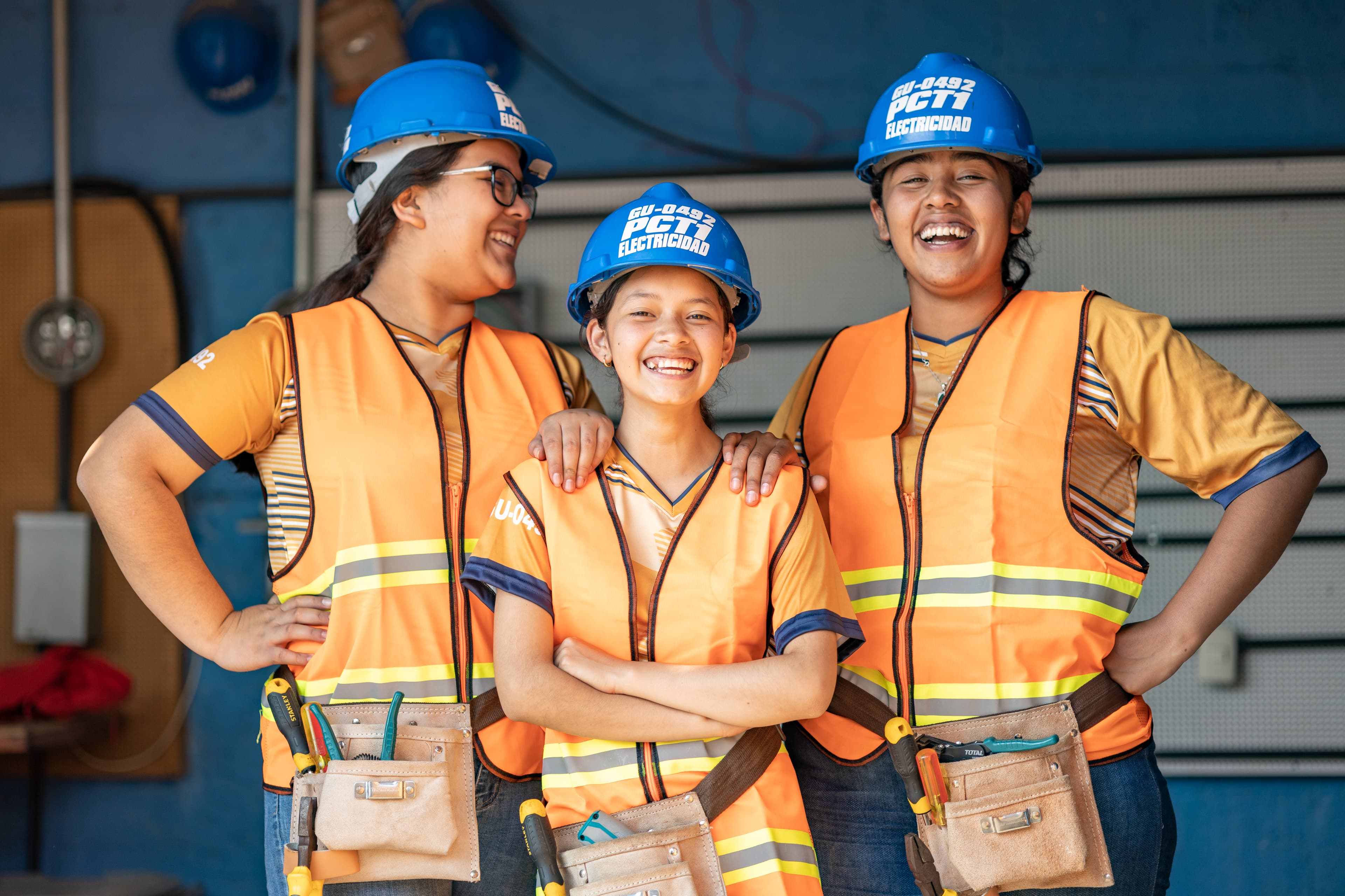 Three young women stand together with their hands on their hips smiling.