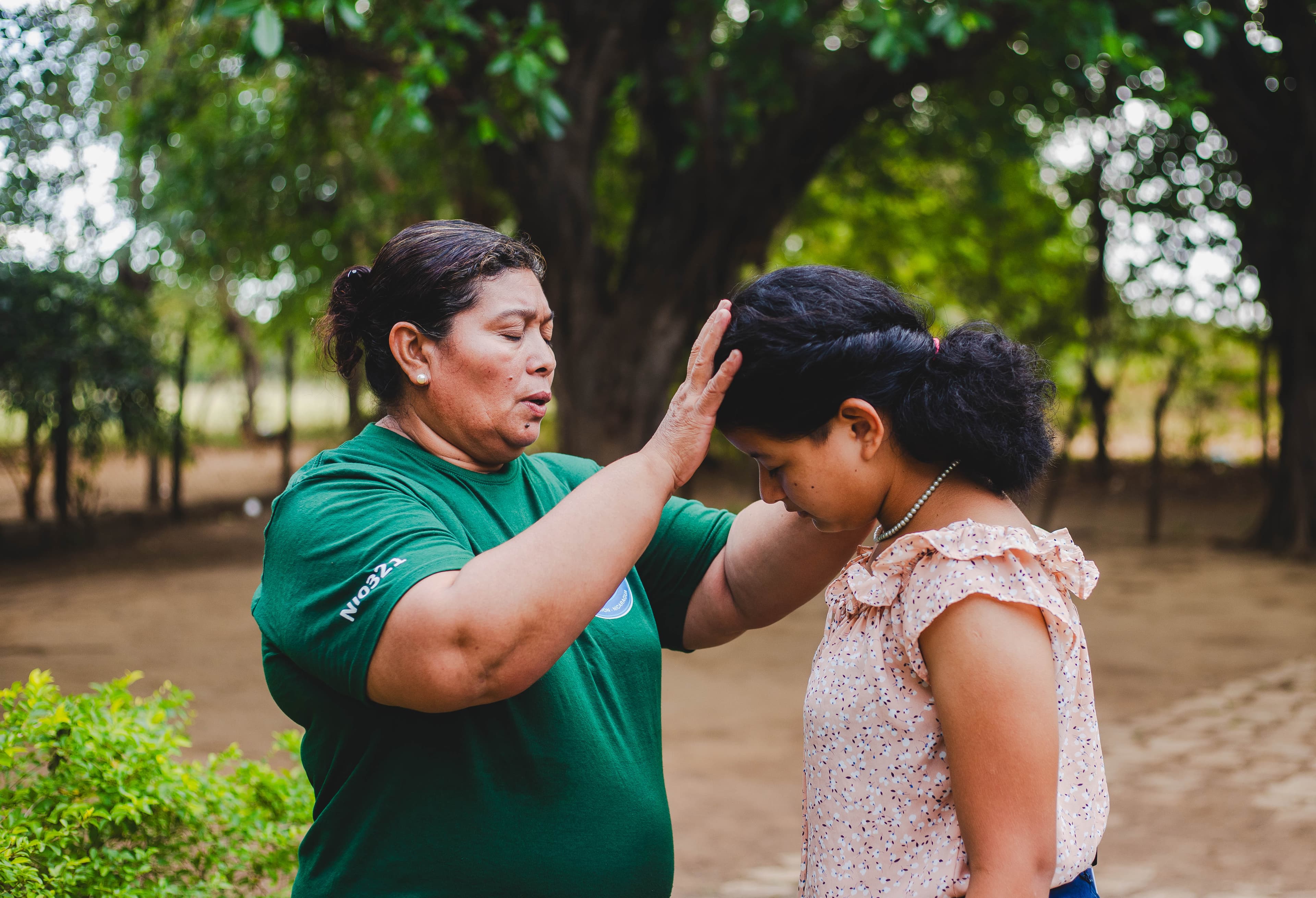 An older woman places her hand on the head of a young girl as they pray.