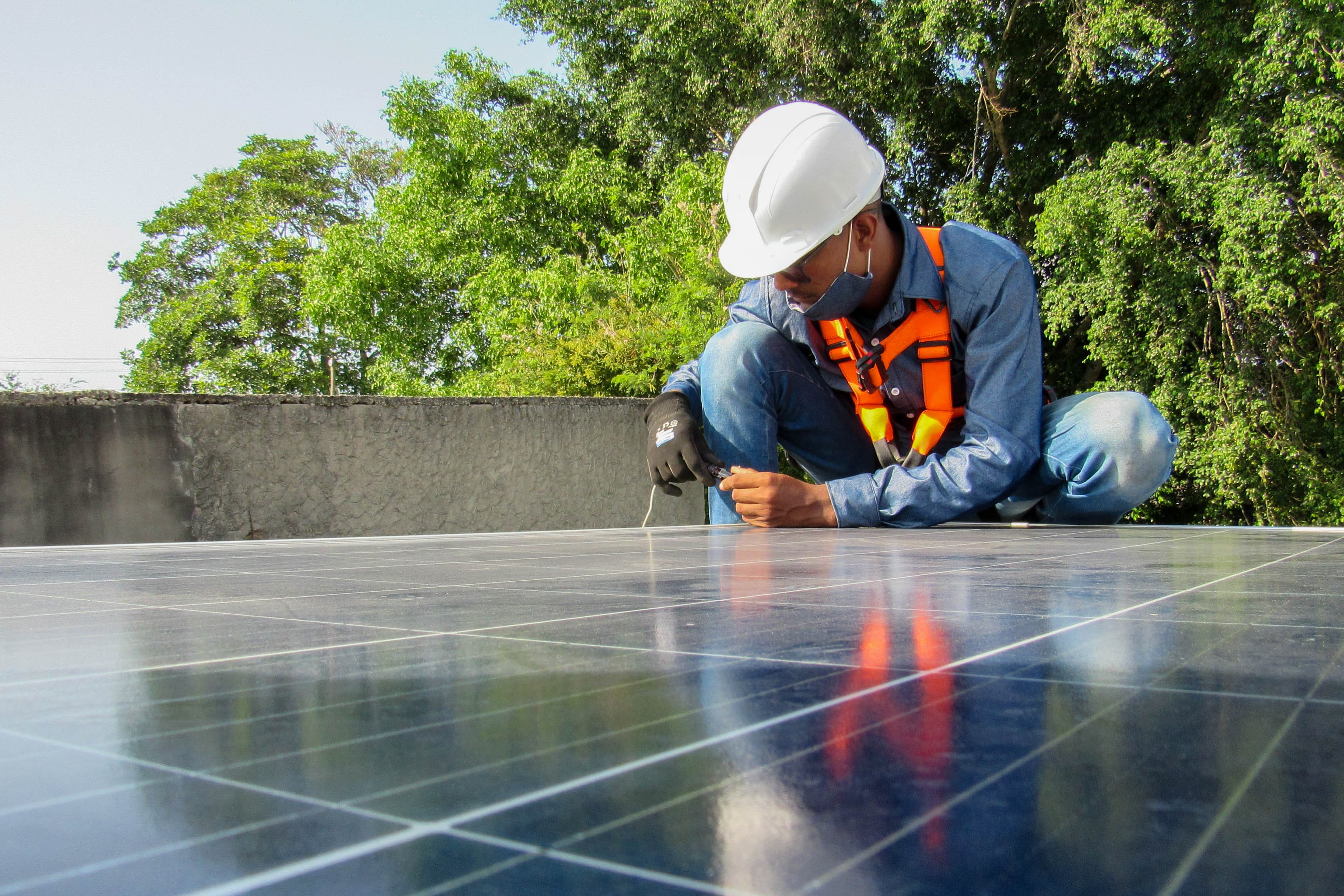 Man is on top of a roof and is installing a solar panel.