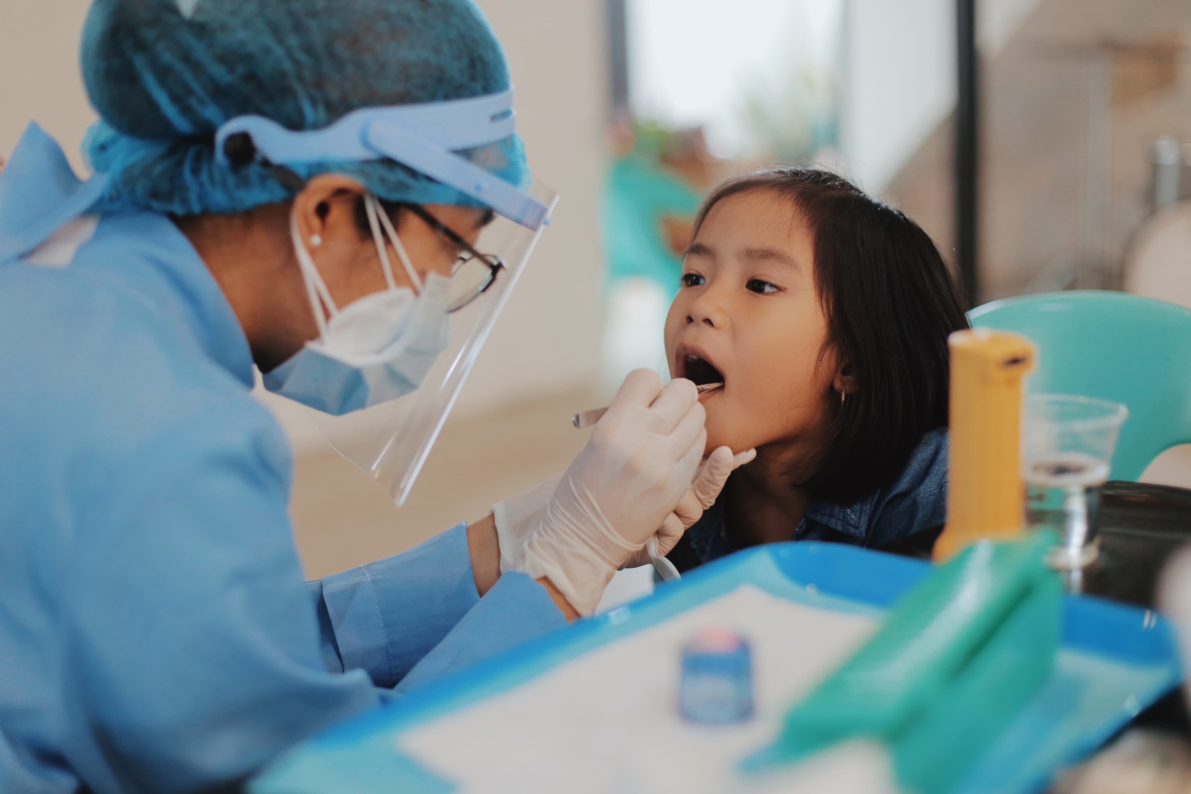 Female dental worker looks in young girl's mouth.