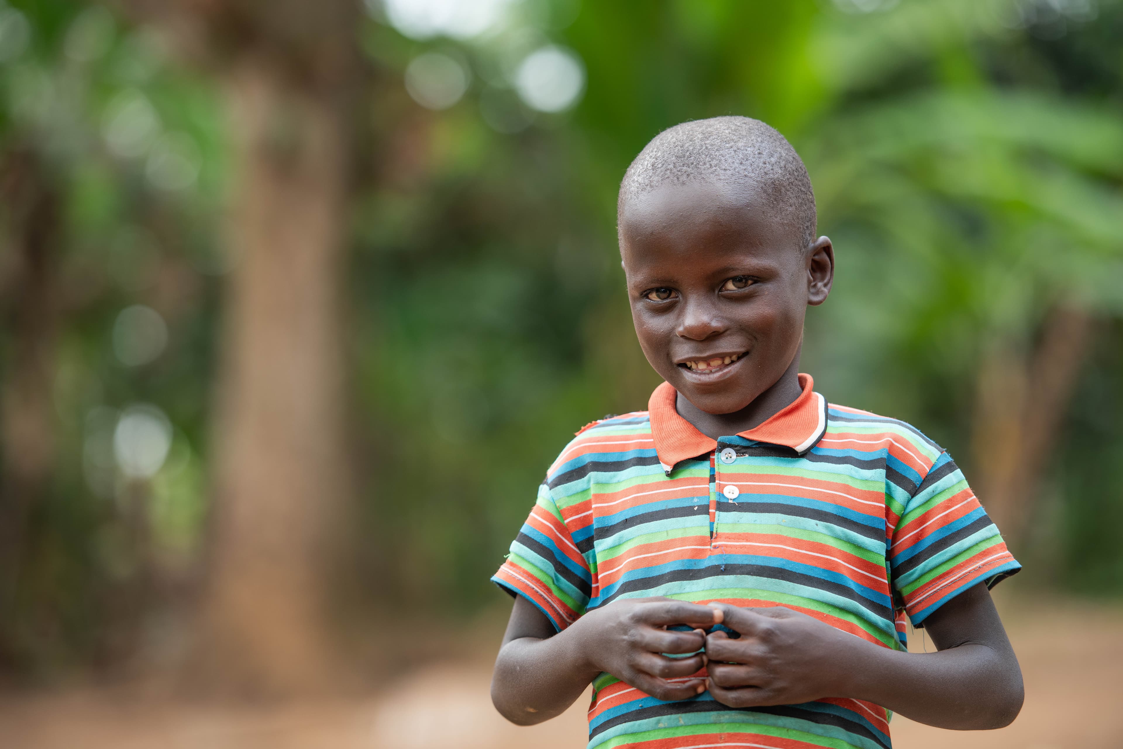 A young boy wearing an orange, green and blue striped polo smiles at the camera.