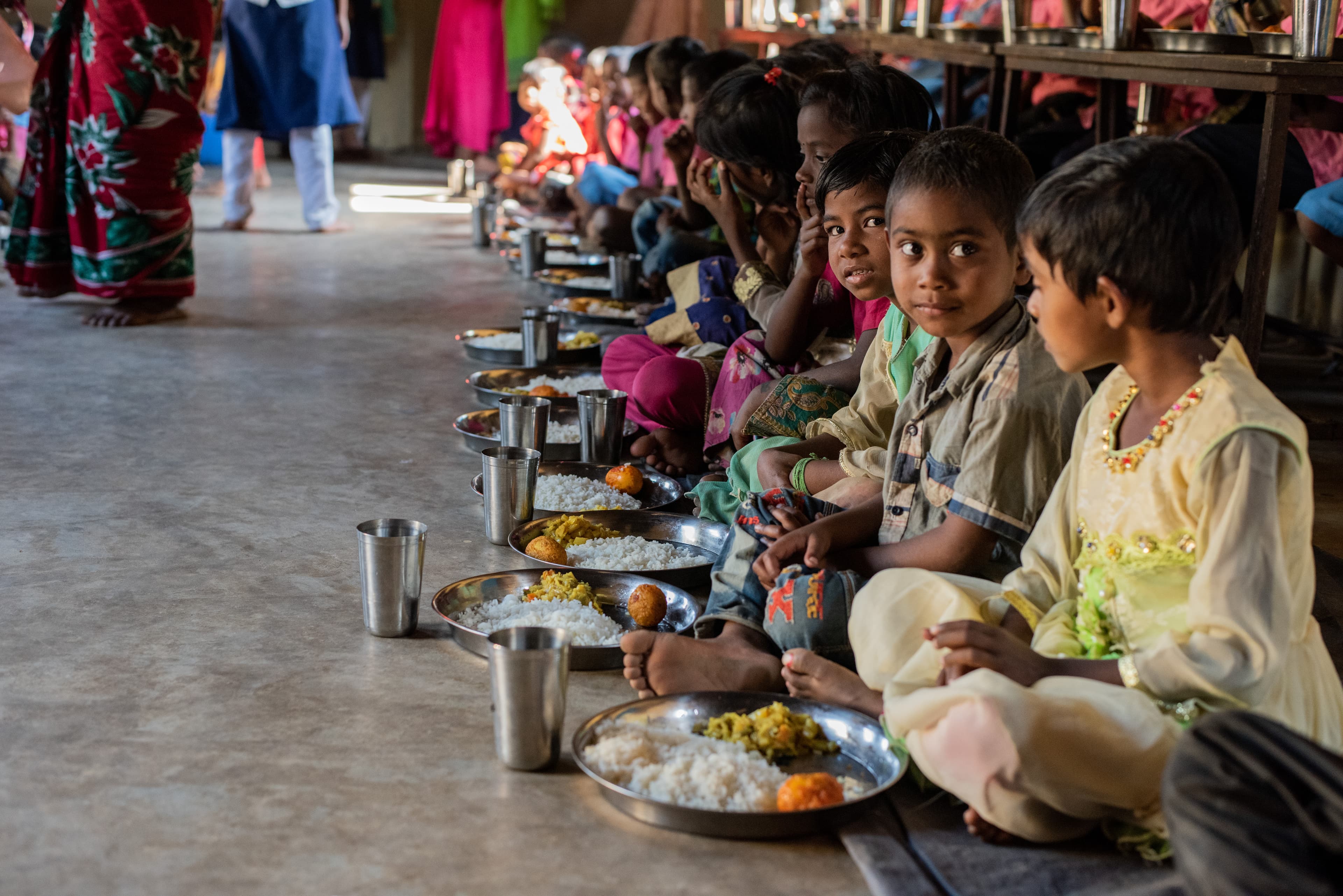 Group of young children sit on the floor eager to eat their meal.