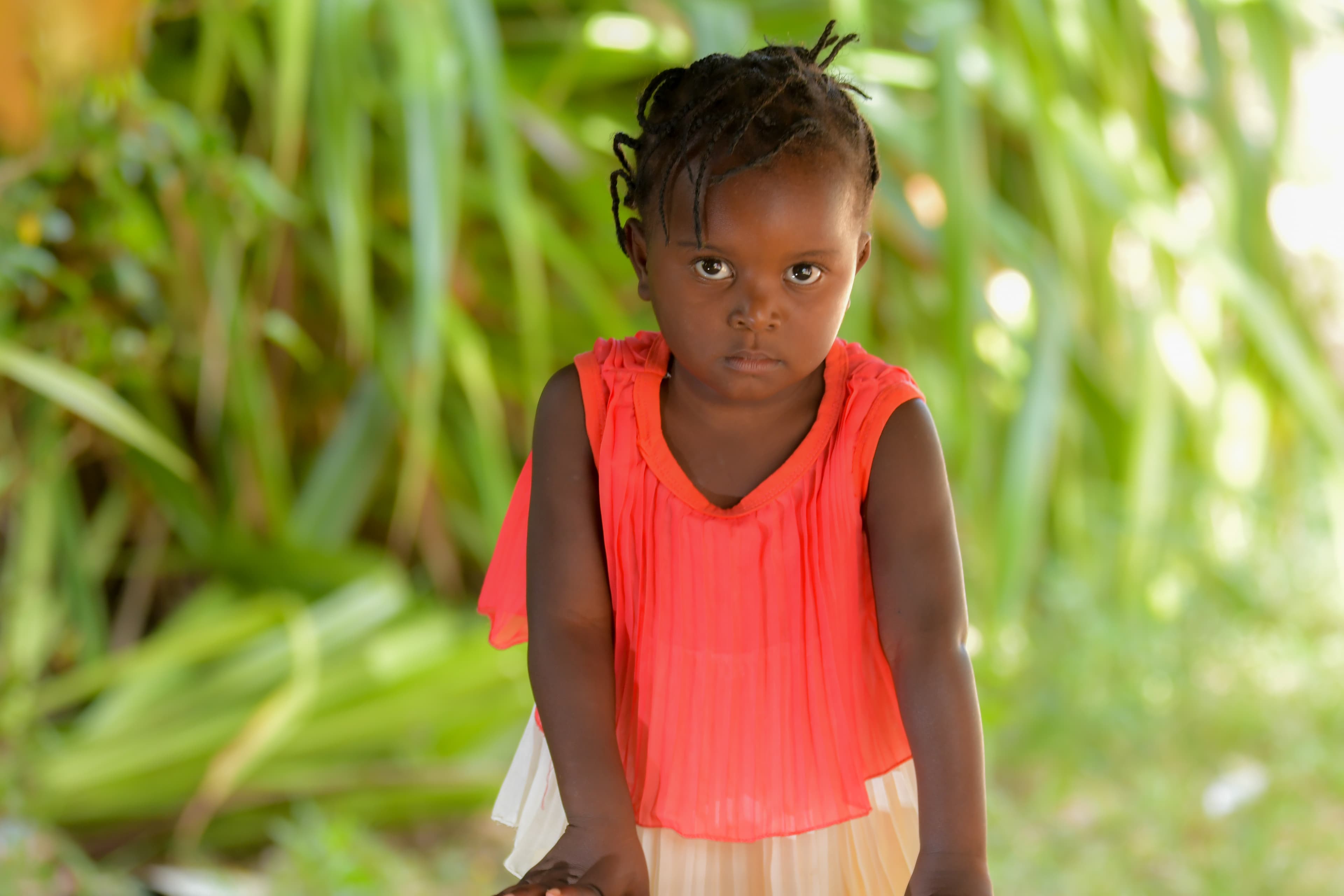A young Haitian girl wearing a red dress looks at the camera with determination.