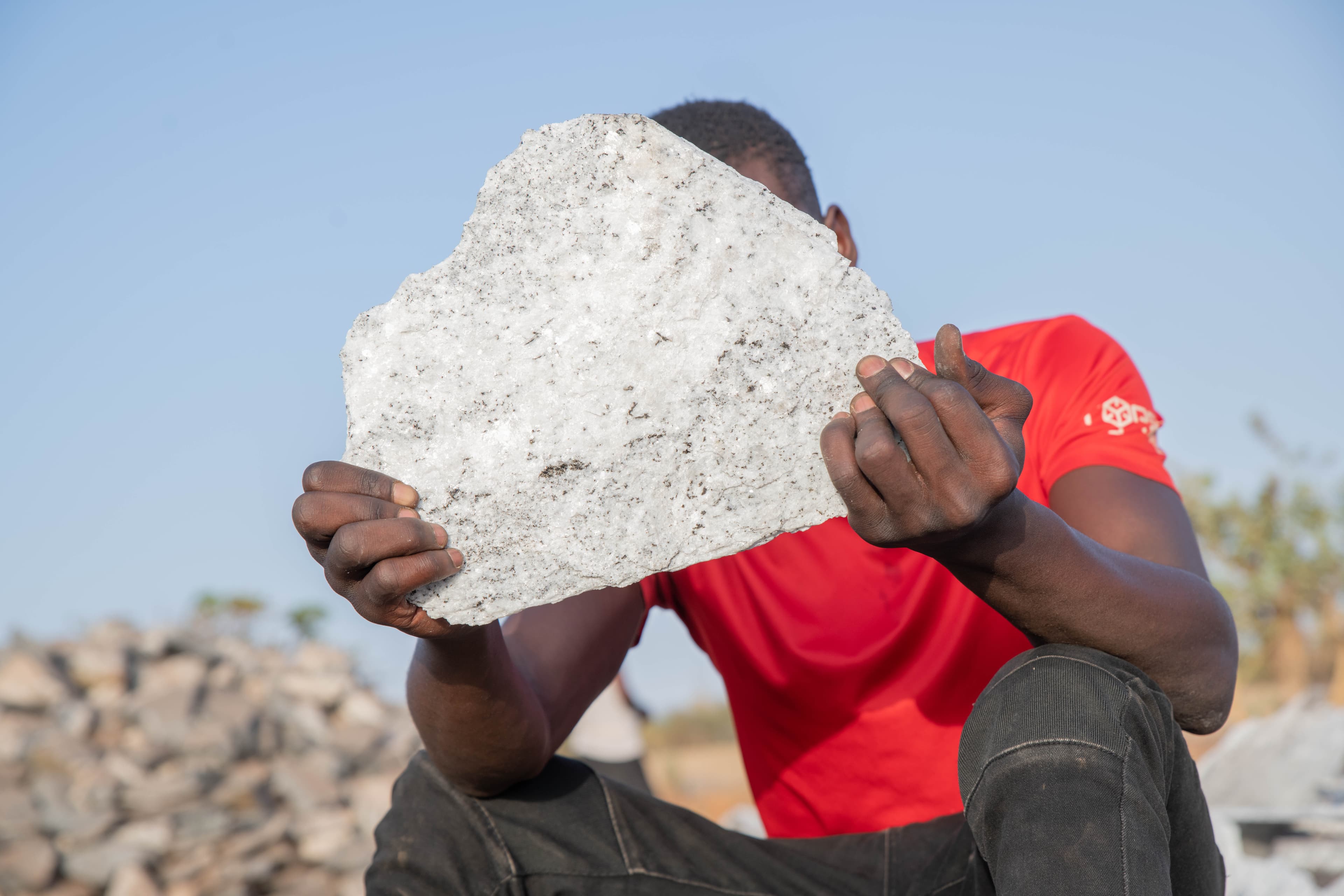 An African teen holds a large piece of white rock over his face.