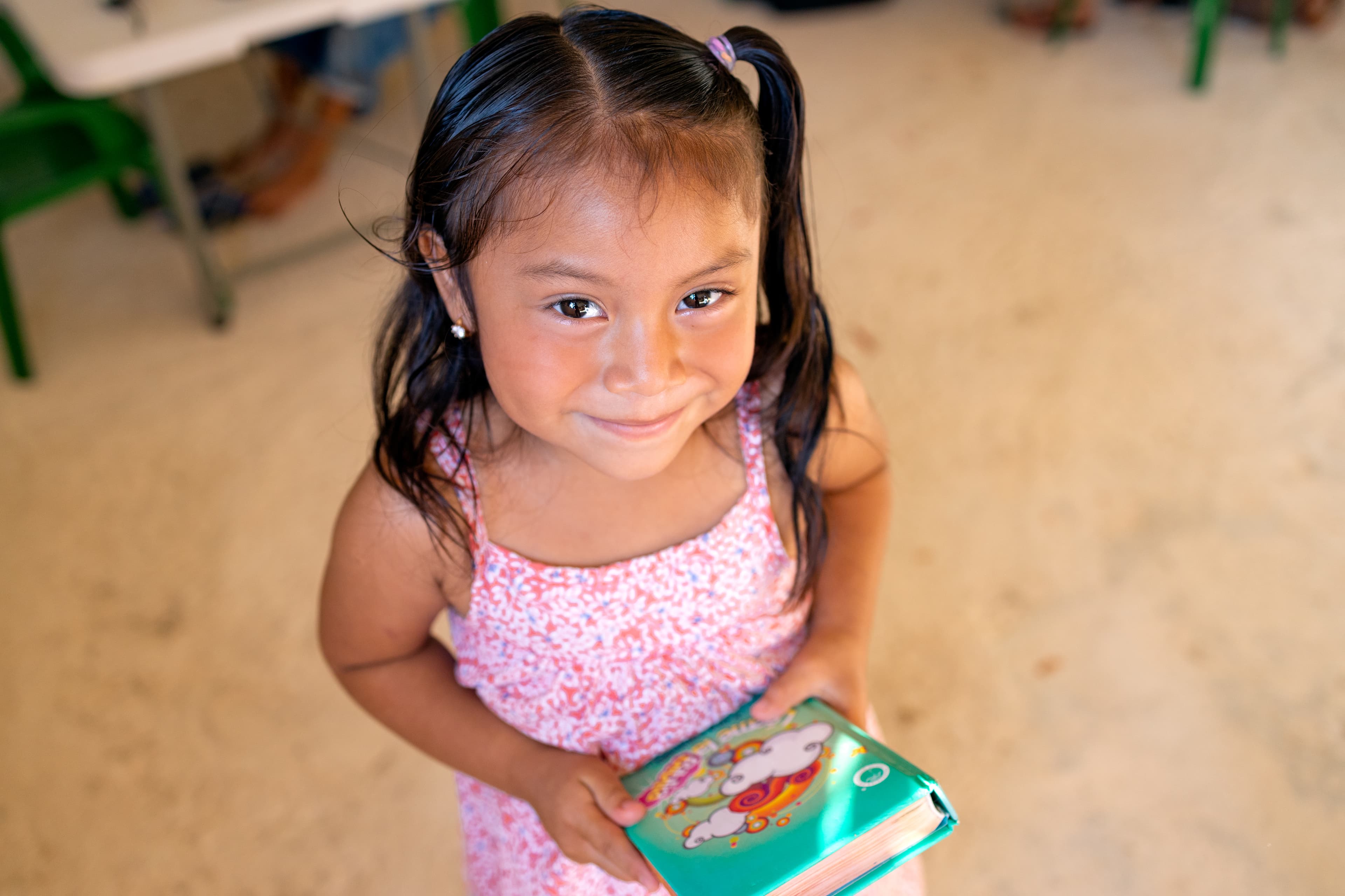 Young girl in pink floral dress smiles while holding a Bible