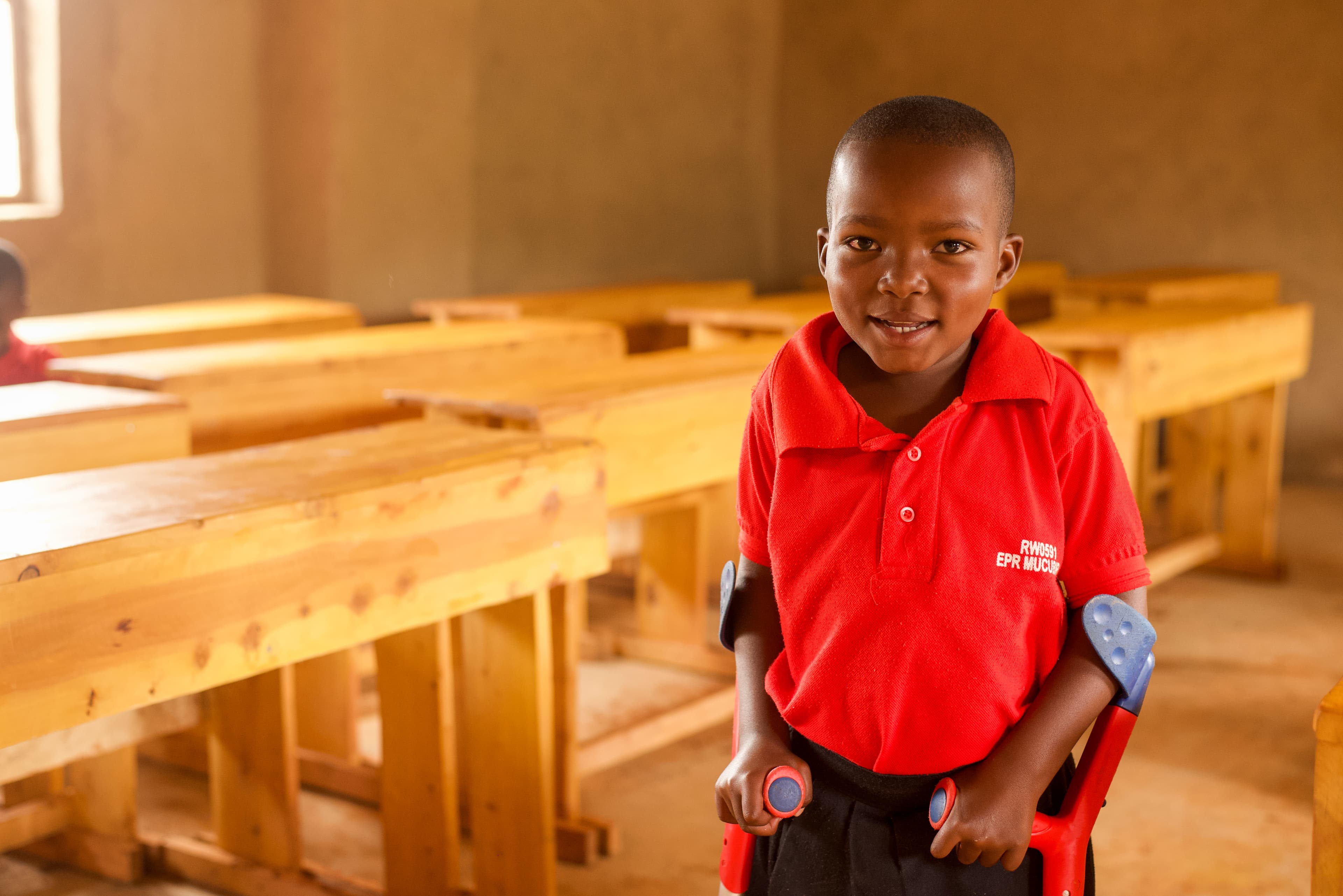 A young girl is standing in a classroom with crutches as she smiles at the camera.
