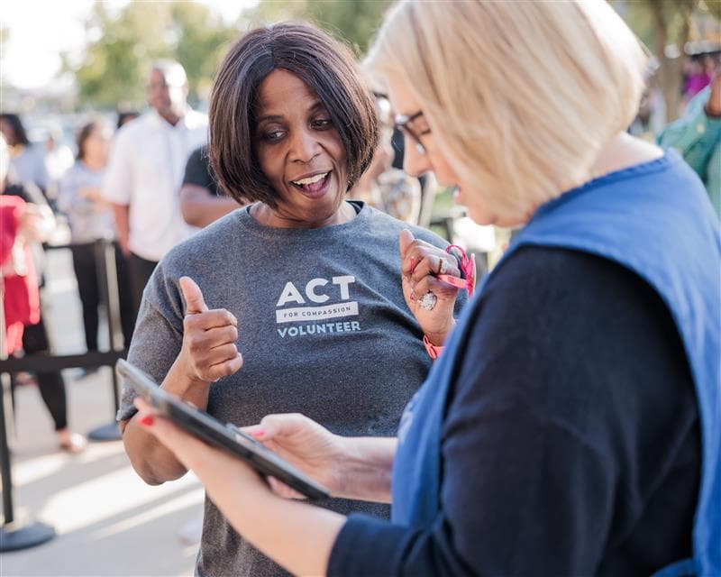 A woman is smiling and giving a thumbs up, wearing a Compassion volunteer shirt.