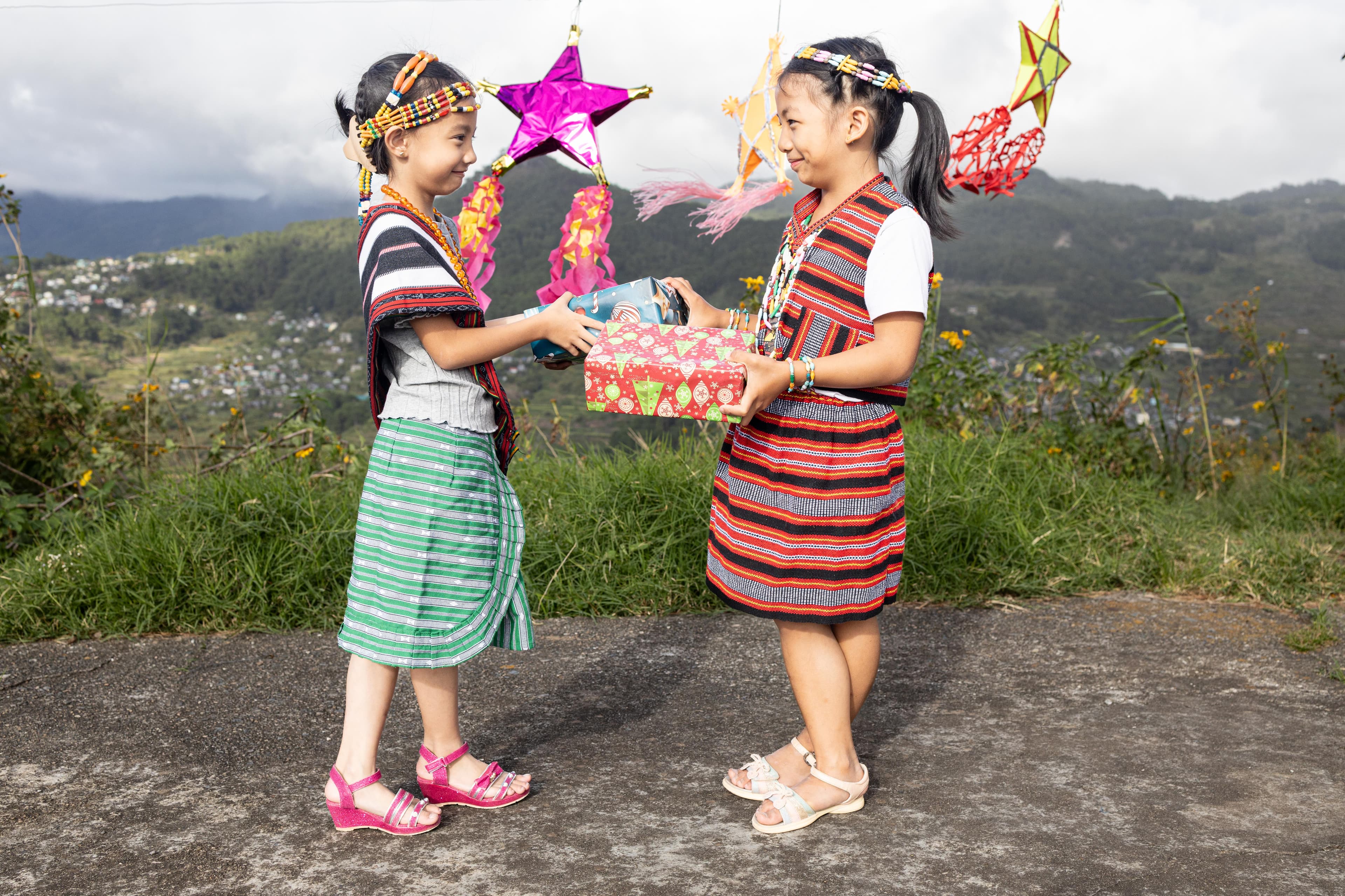 Two young girls are dress up for Christmas holding gifts and smiling.