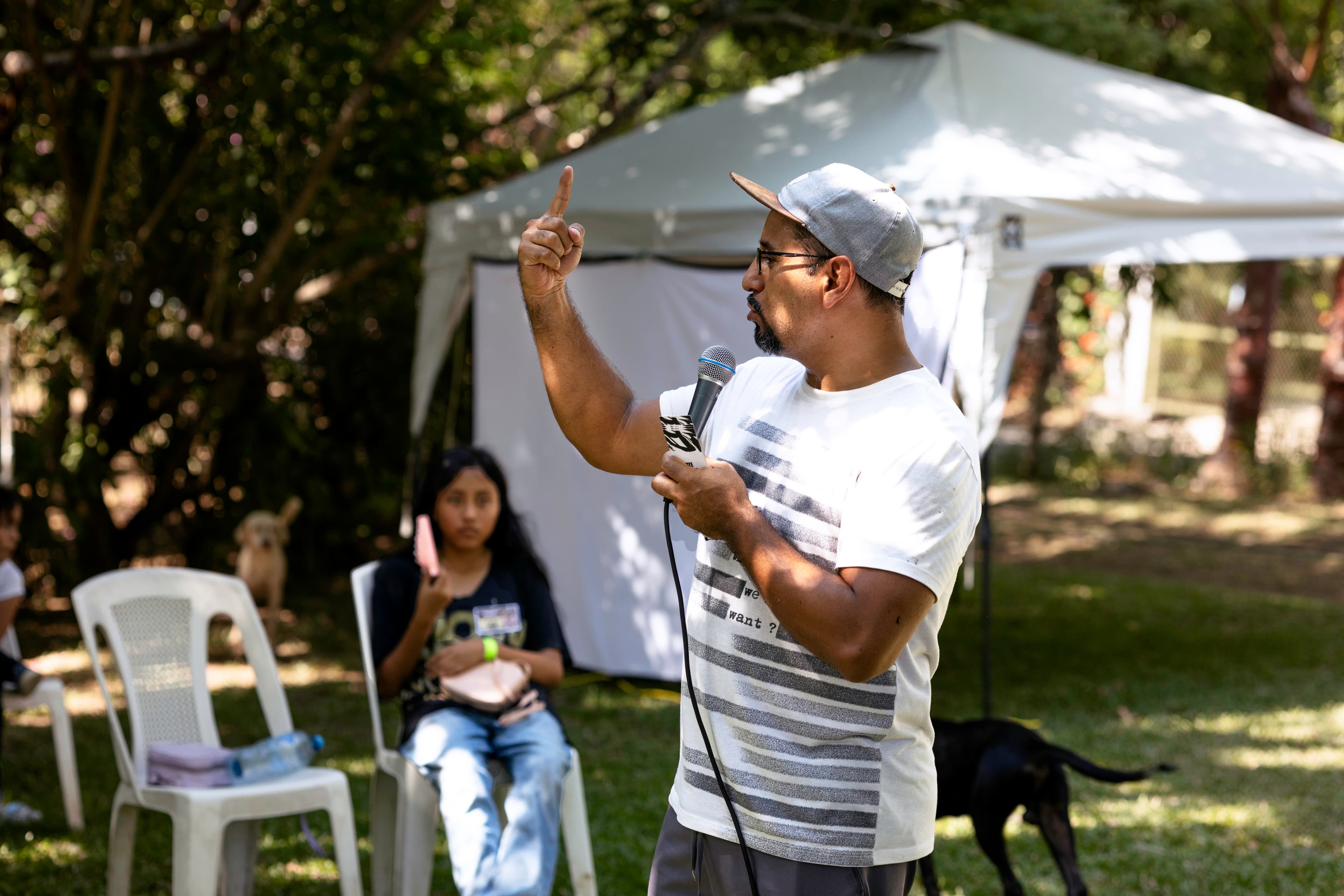 An older man holds a microphone while pointing to the sky.