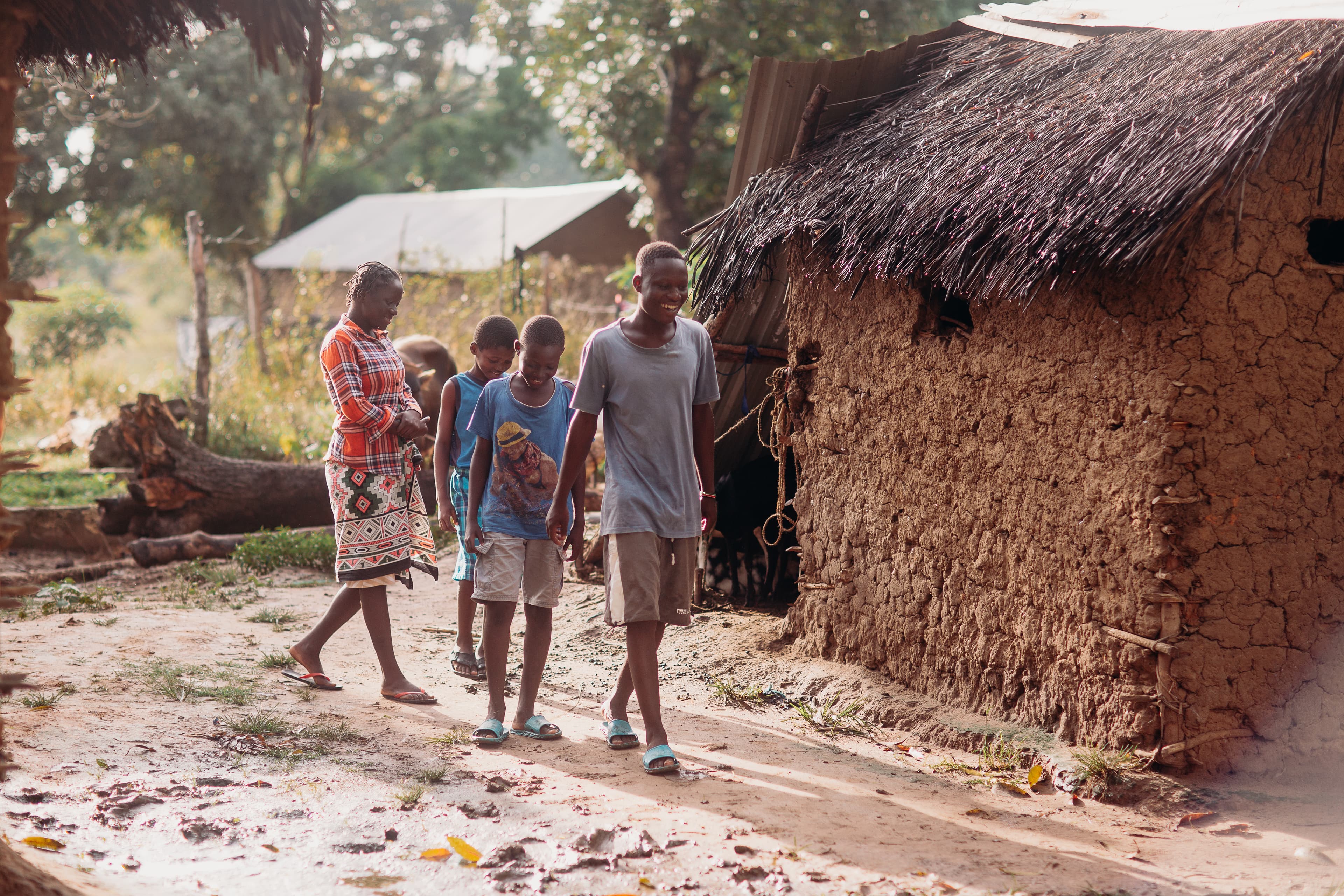 A teen African boy walks in front of his two siblings and his mother while smiling.