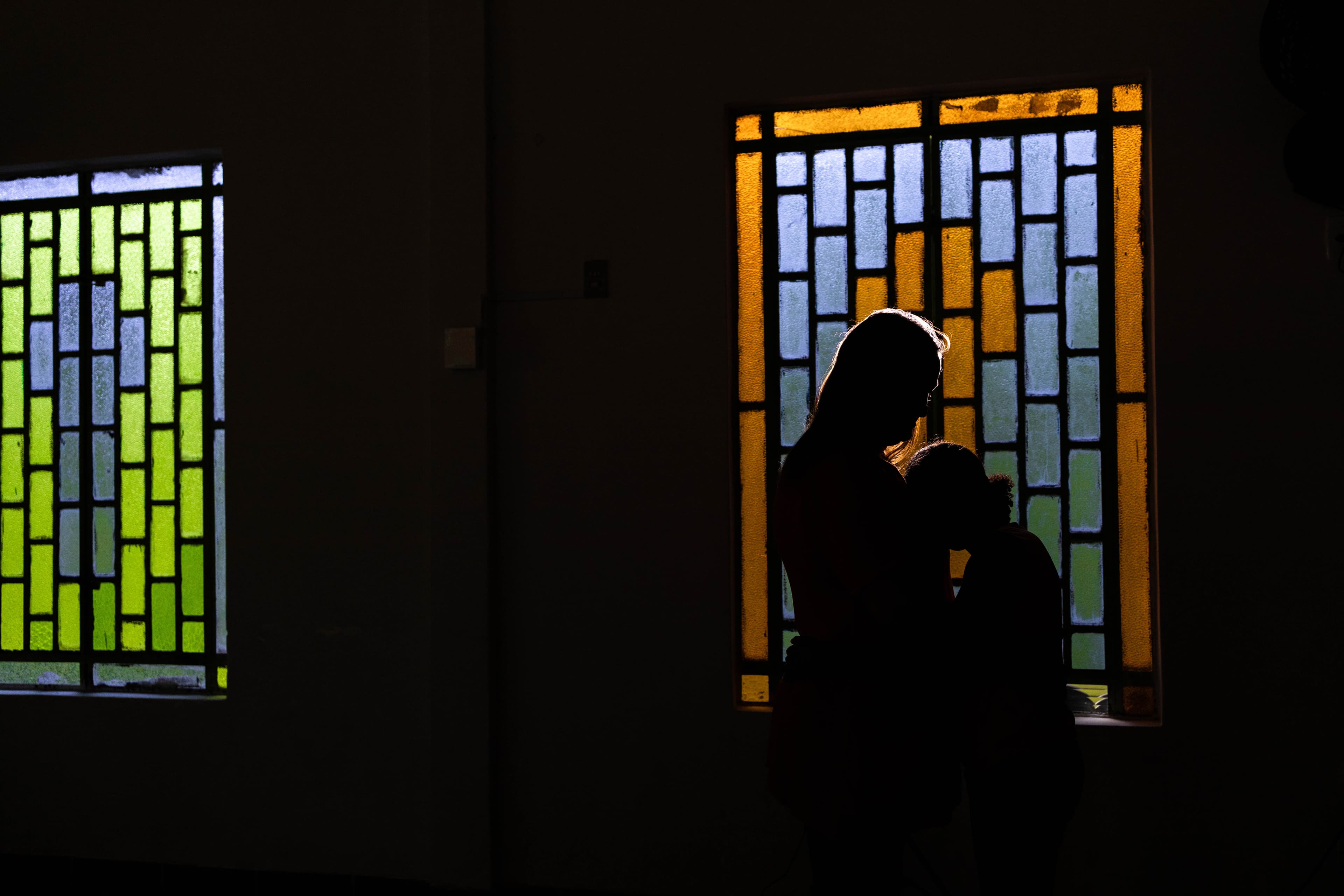 A silhouette of an older woman and young girl in front of a stained glass window.