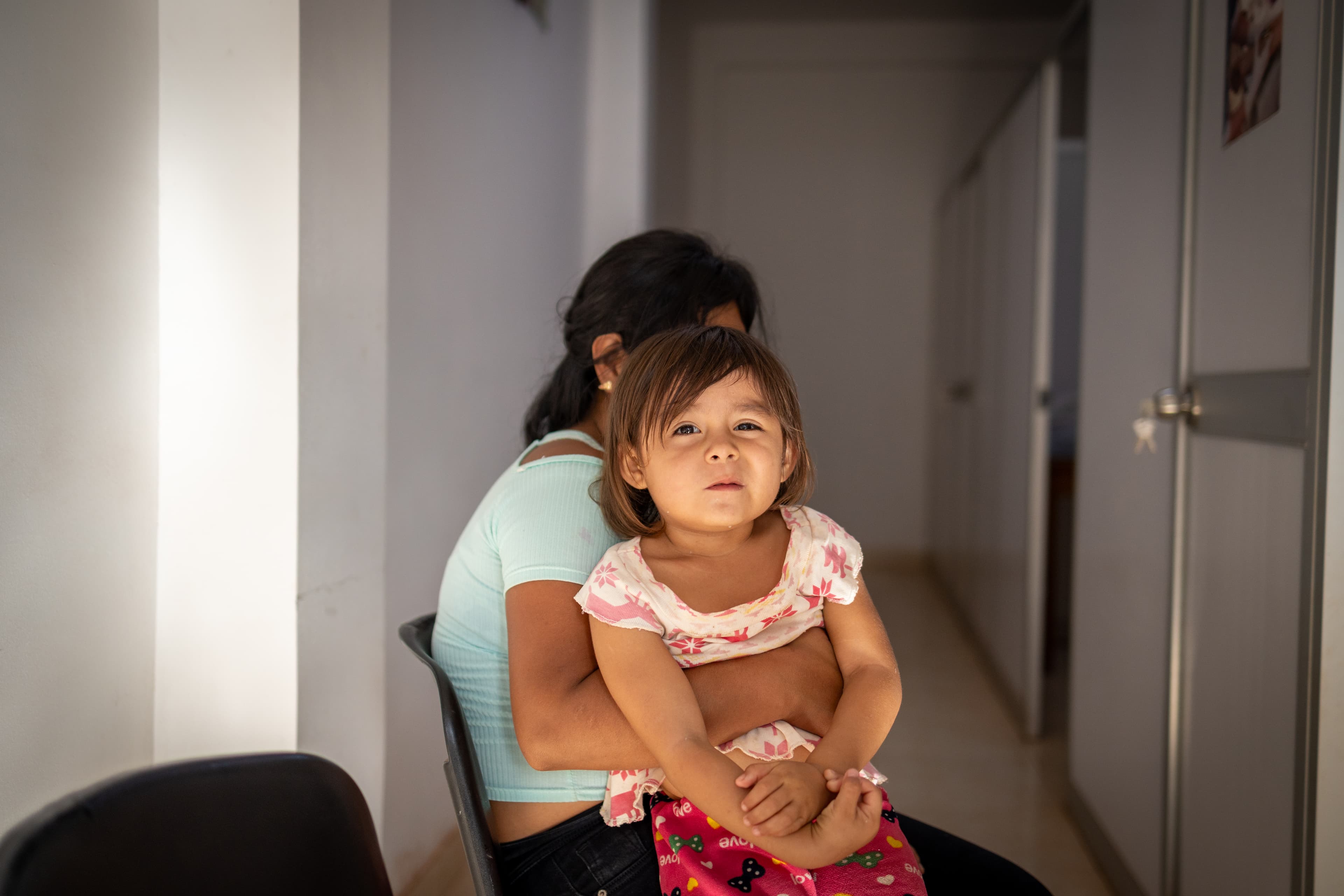 A young girl sits on her mother’s lap while looking at the camera.