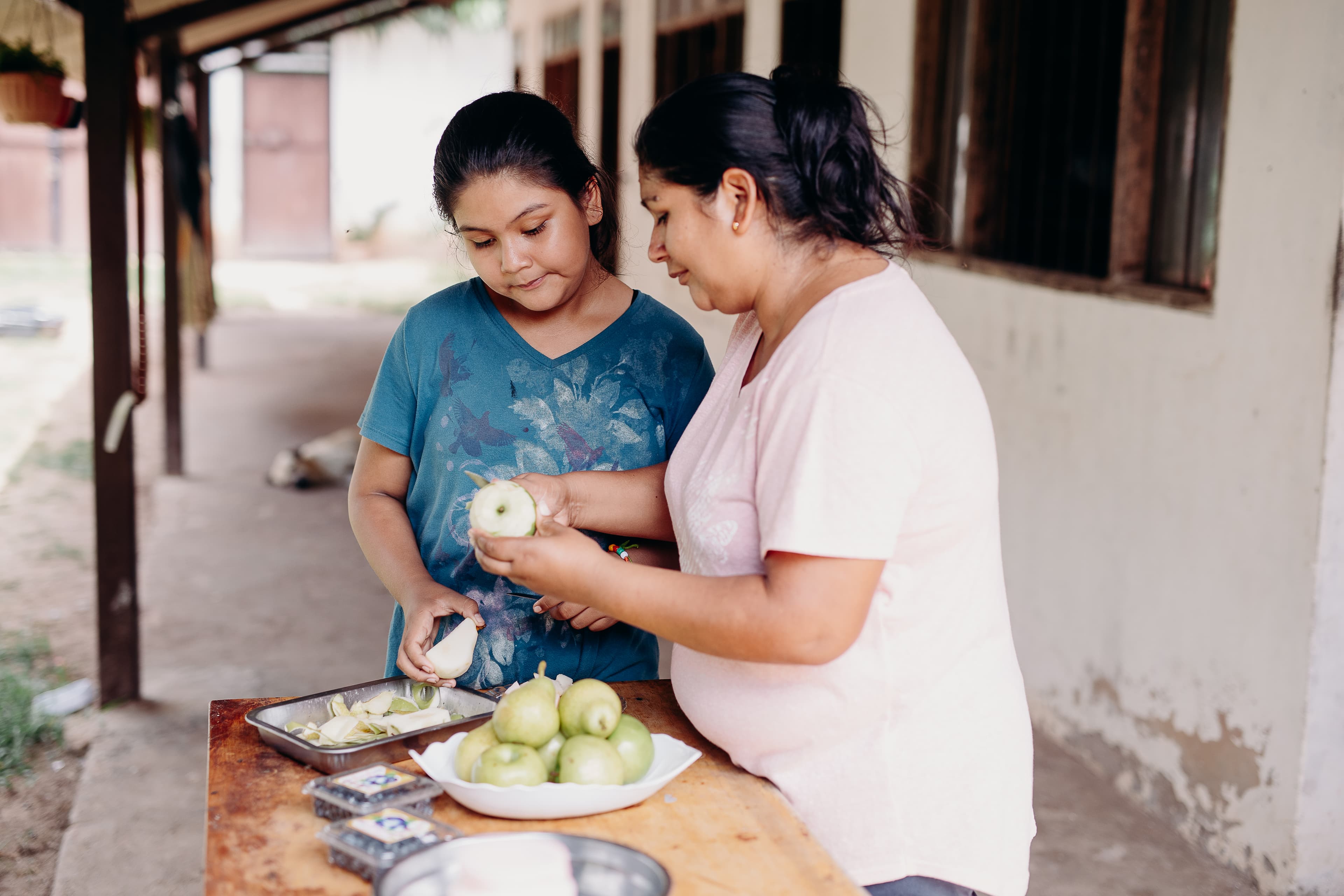 A young girl and her mother stand at a table peeling apples.